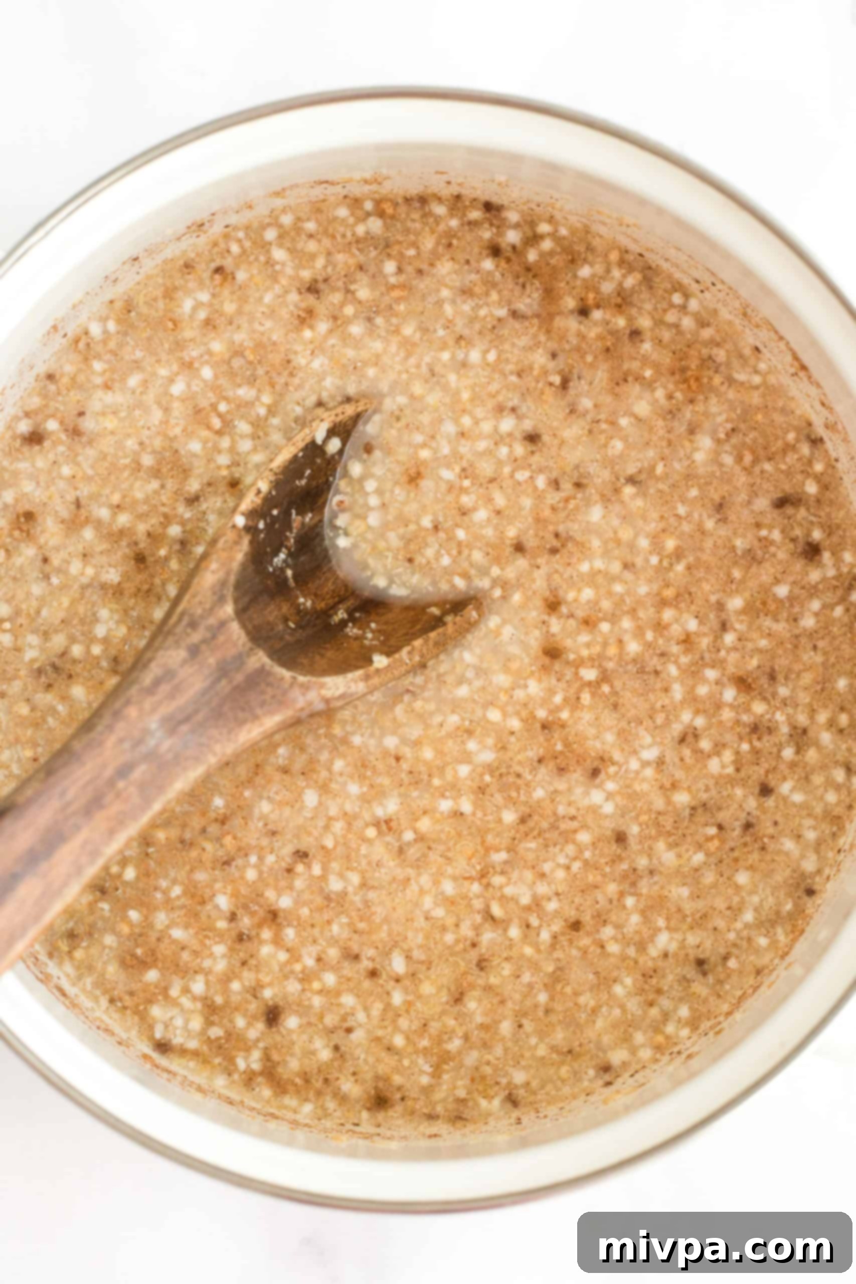 Adding almond milk and water to the dry quinoa flake mixture in a white pot, preparing it for cooking.