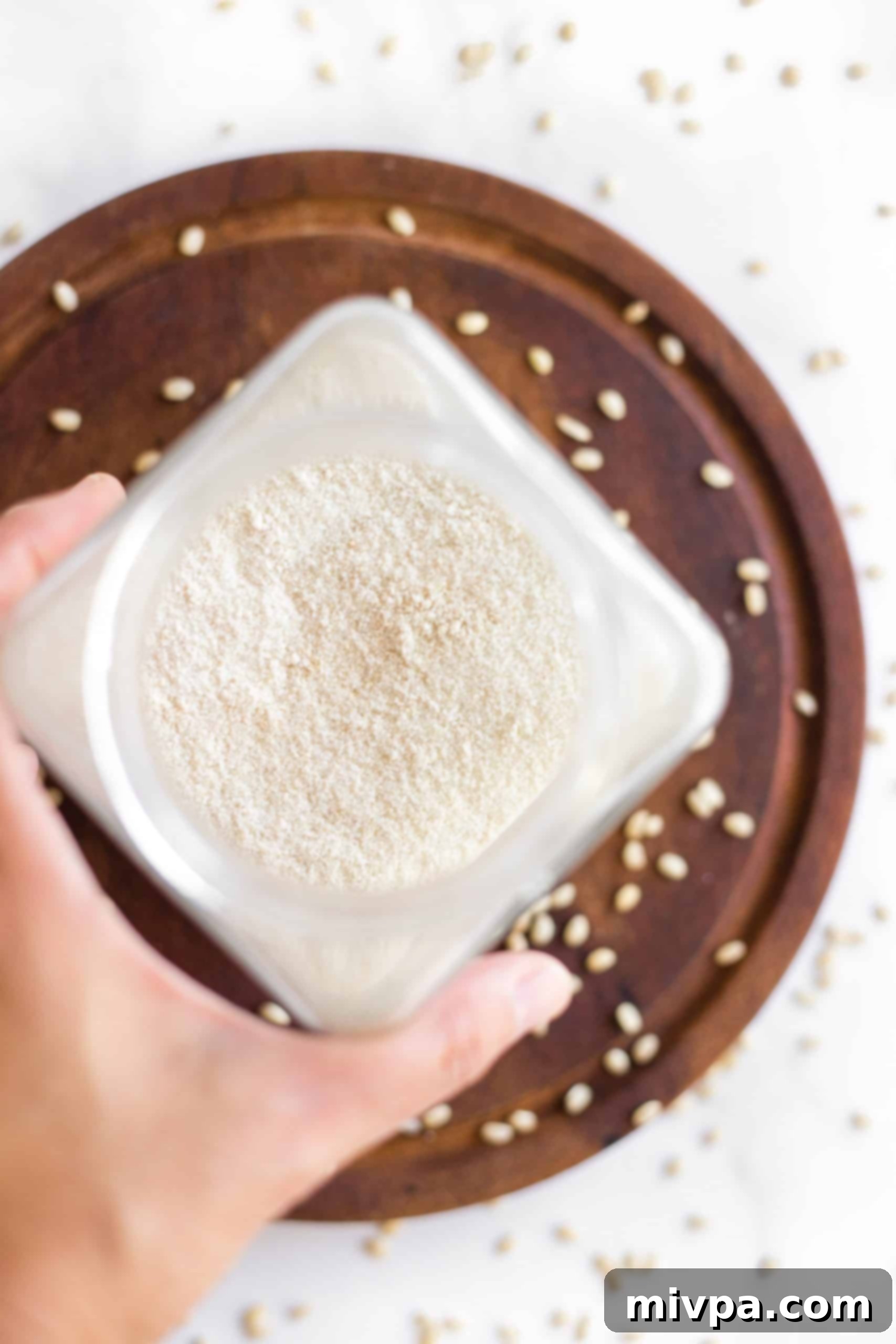 Fine brown rice flour in a glass jar, surrounded by uncooked brown rice grains on a rustic wooden board.