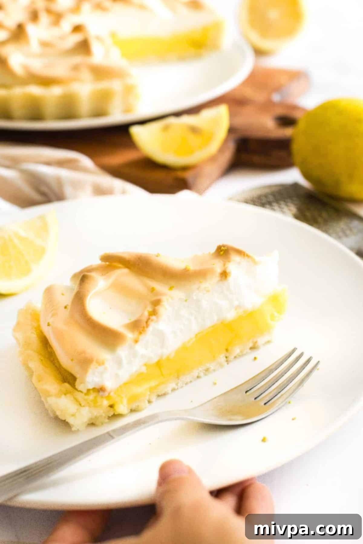Hand reaching for a plate of gf lemon meringue pie.