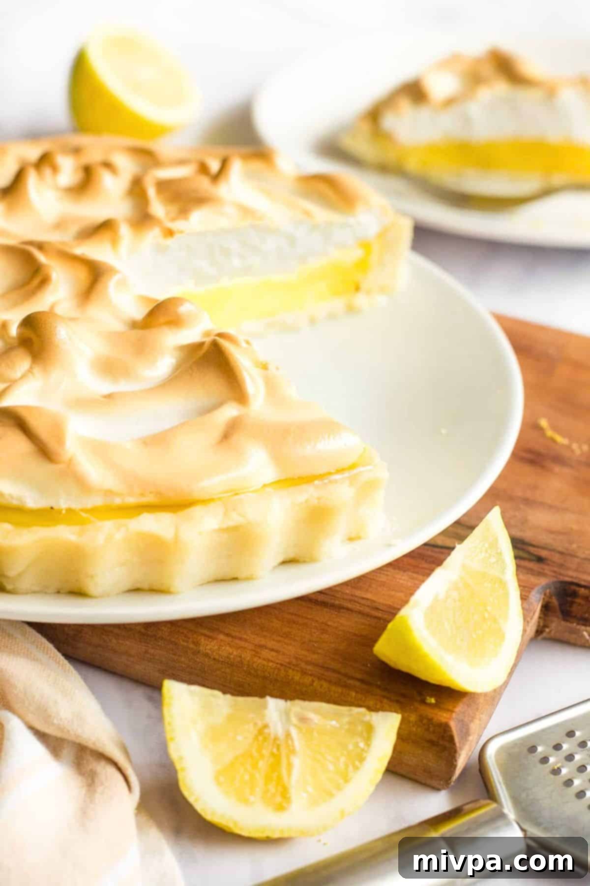 Half-eaten gf lemon meringue pie on wooden board.