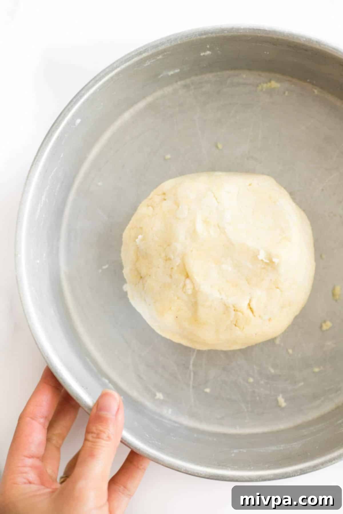 Hand holding a metal bowl with a ball of pie crust dough.