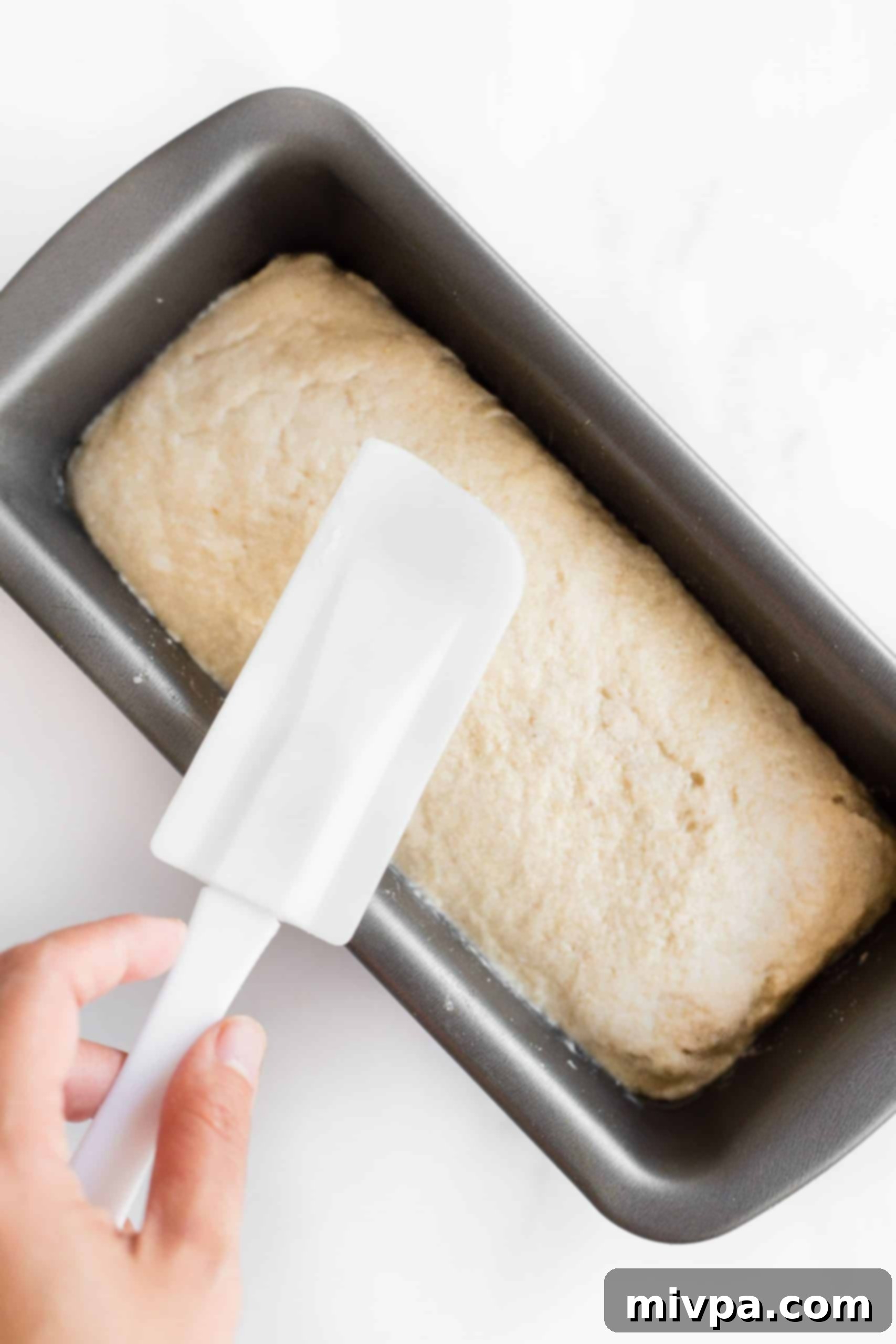 Using a spatula to smooth out the top of brown rice bread dough in a pan.