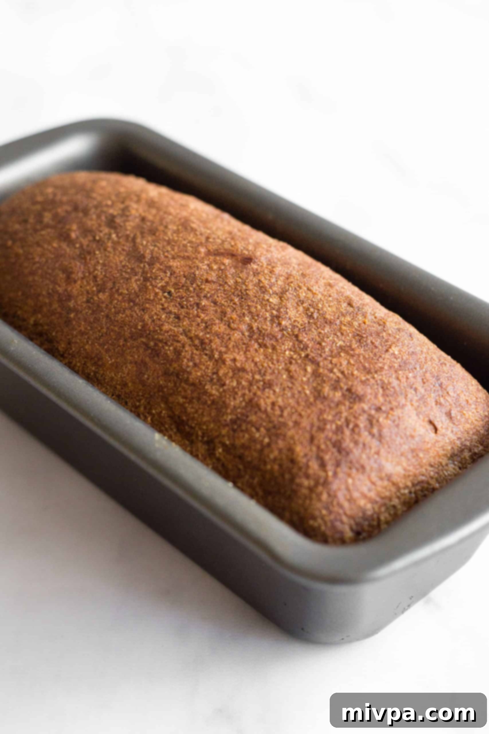 A just-baked loaf of soft, fluffy brown rice bread in a metal pan.