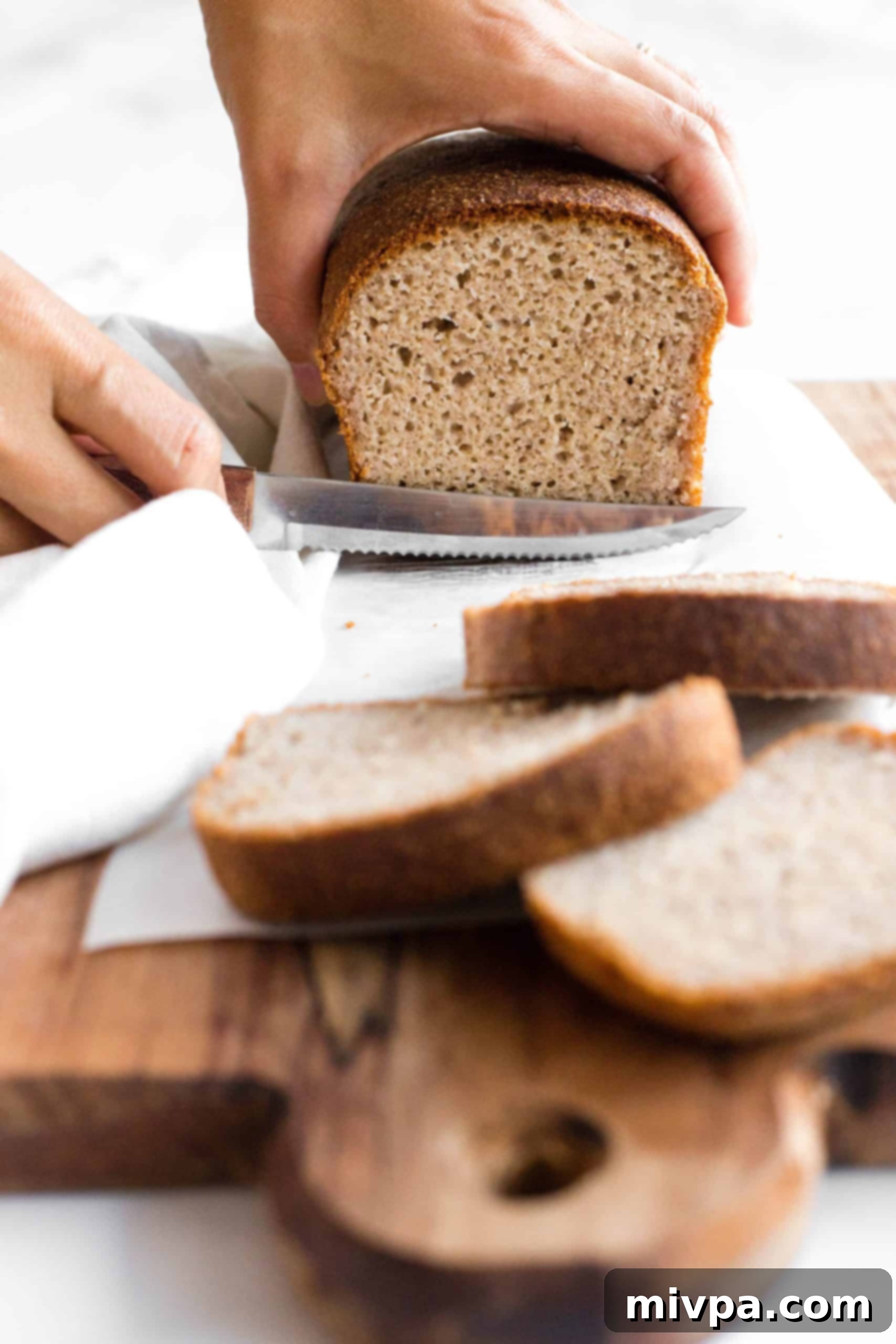 Hand slicing into a loaf of gluten-free brown rice bread.