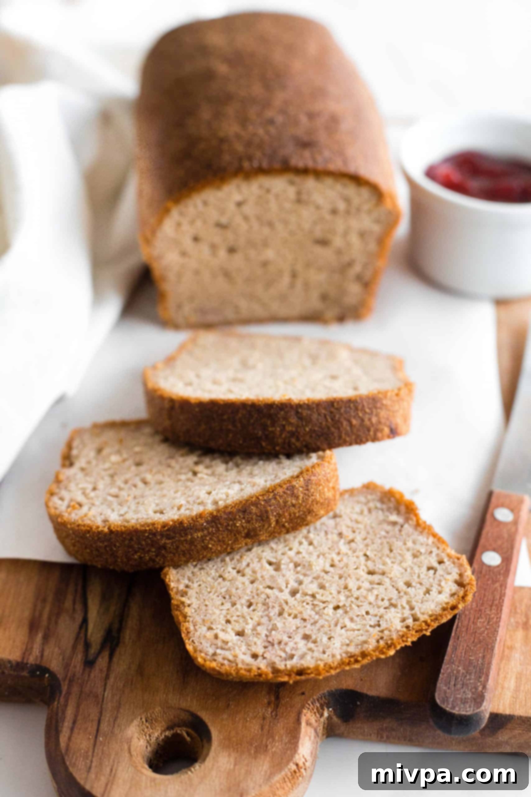 Sliced loaf of soft, fluffy brown rice bread on parchment-lined board.