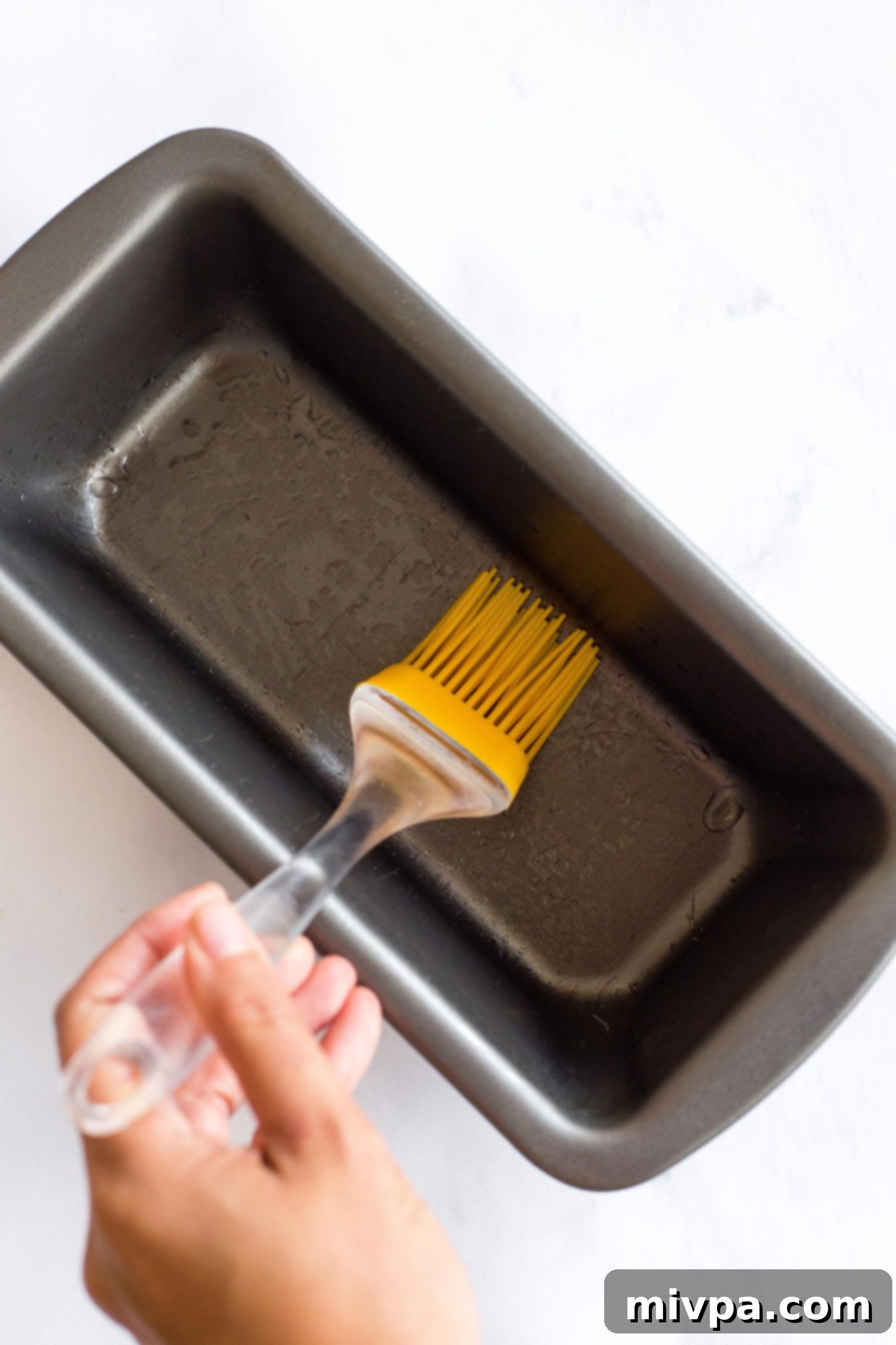 Greasing a metal loaf pan with cooking spray.