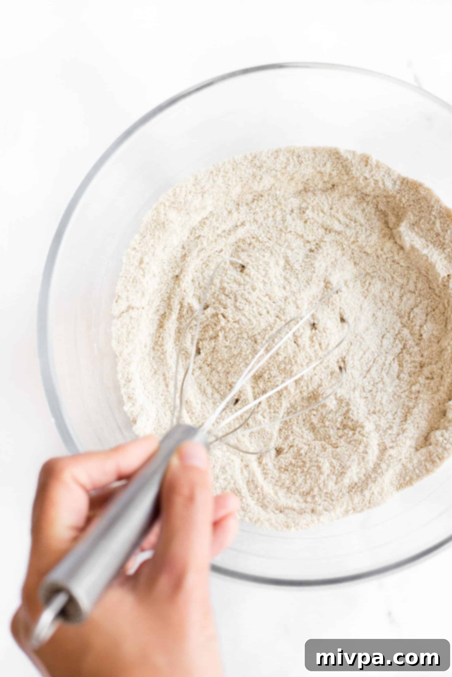 Whisking dry ingredients in a large glass bowl for brown rice bread.
