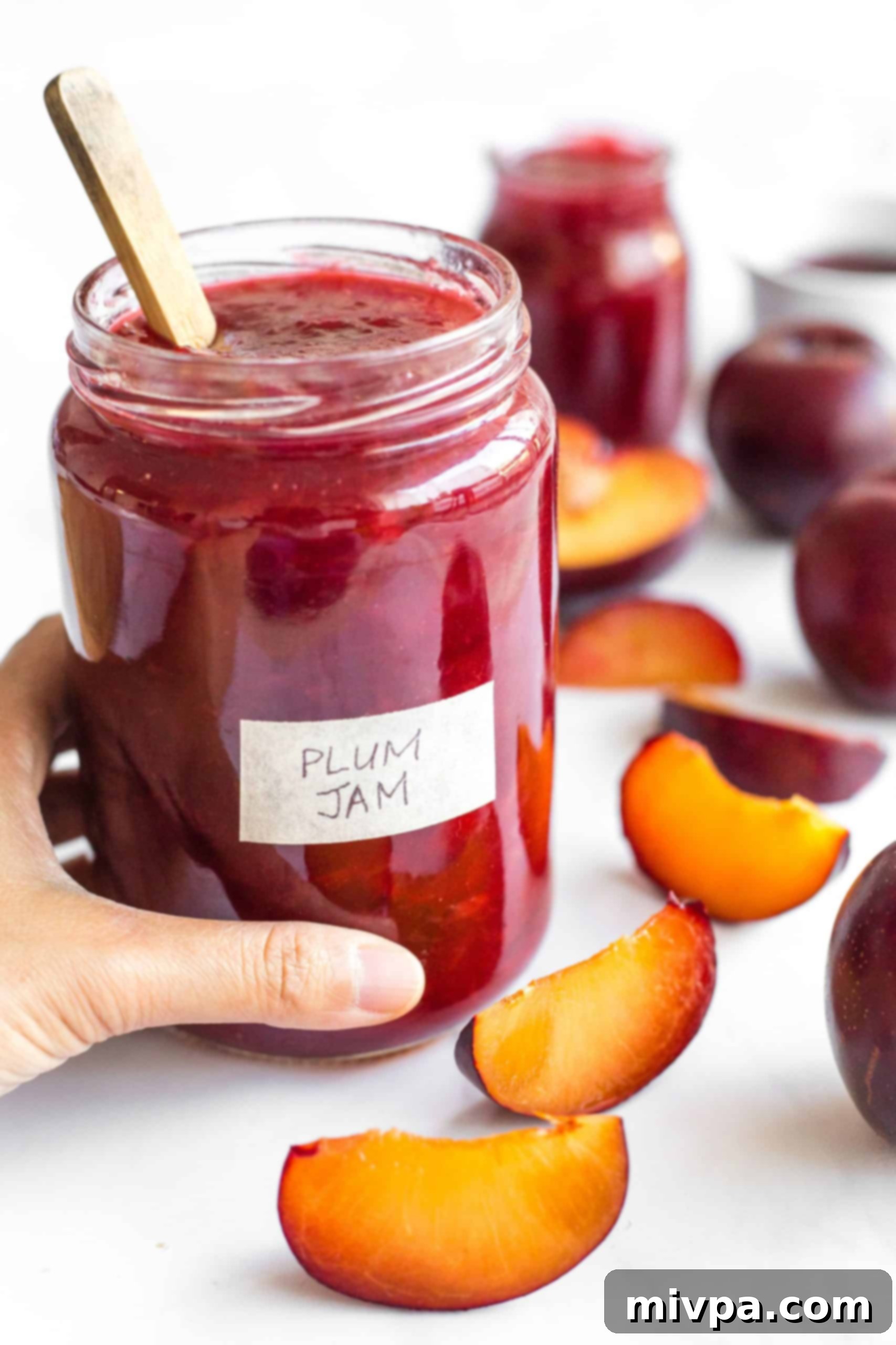Easy Plum Jam Recipe (No Pectin) Hand holding a jar of vibrant red plum jam, homemade and ready to enjoy.