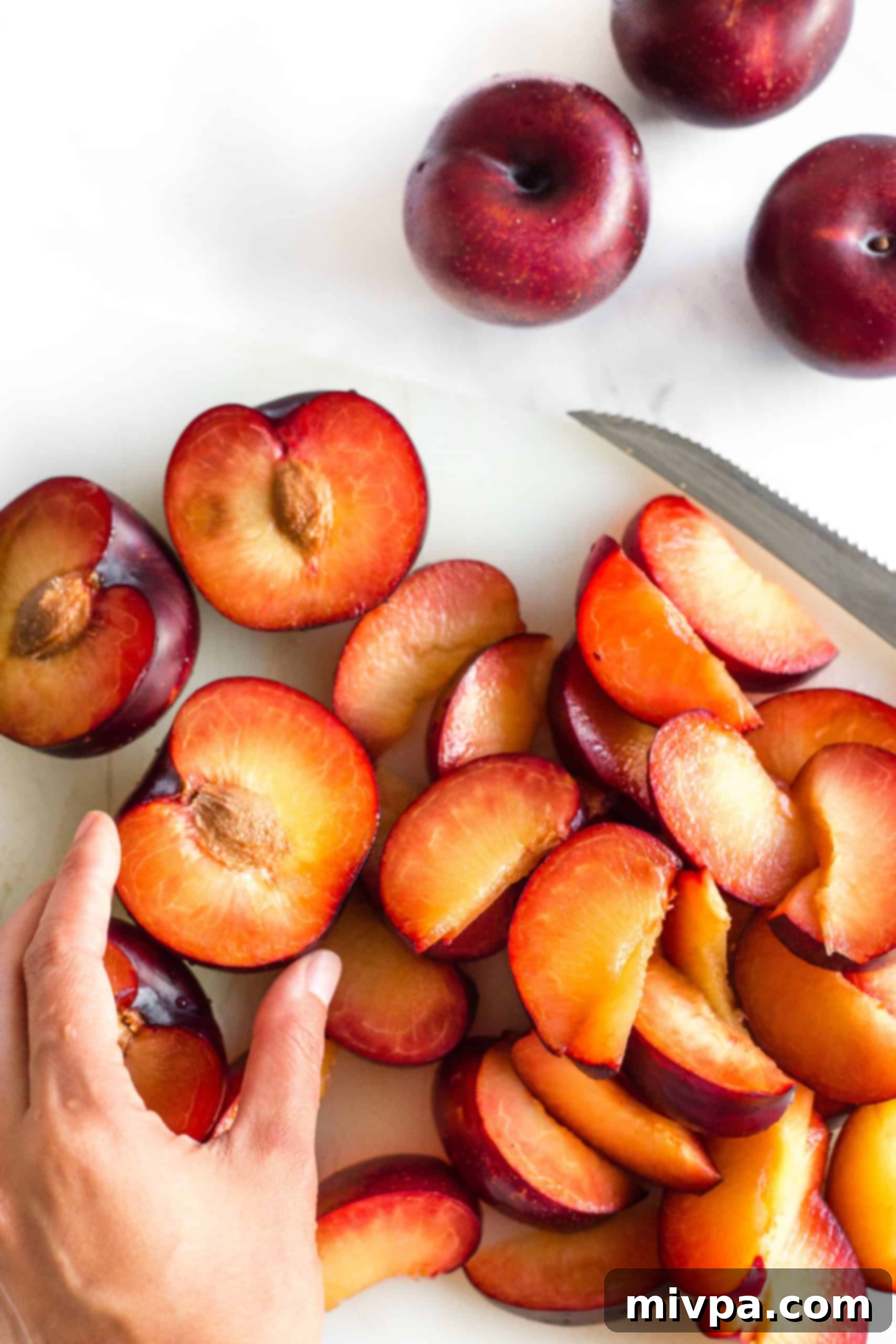 Easy Plum Jelly Without Pectin (Gluten-Free, Vegan) A hand reaching for beautifully sliced plums arranged on a clean chopping board, ready for the next step in jam making.