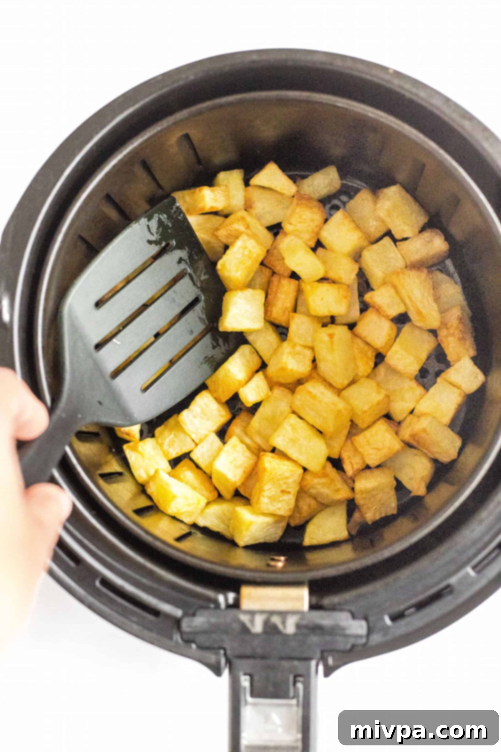 Tossing air fryer diced potatoes in an air fryer basket.