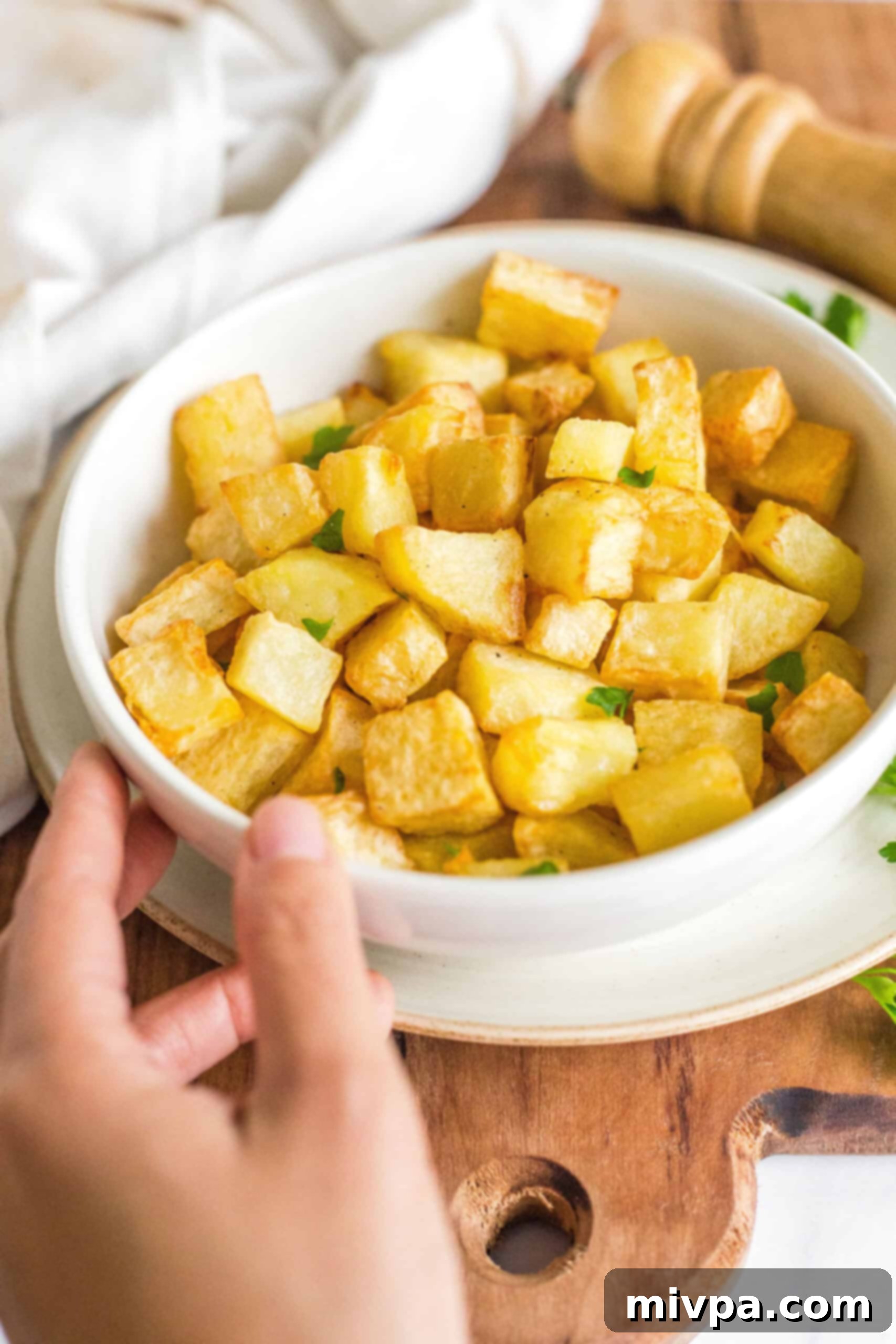 Hand holding a bowl of air fried potatoes.