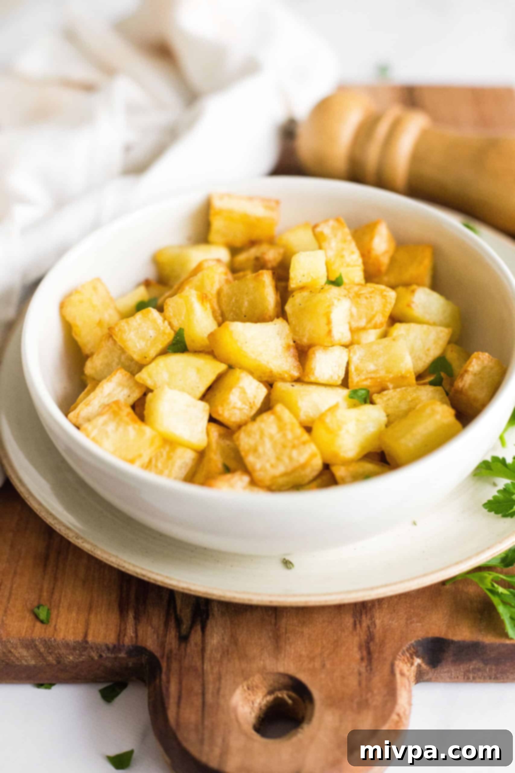 A bowl of air fried diced potatoes on a wooden board. 