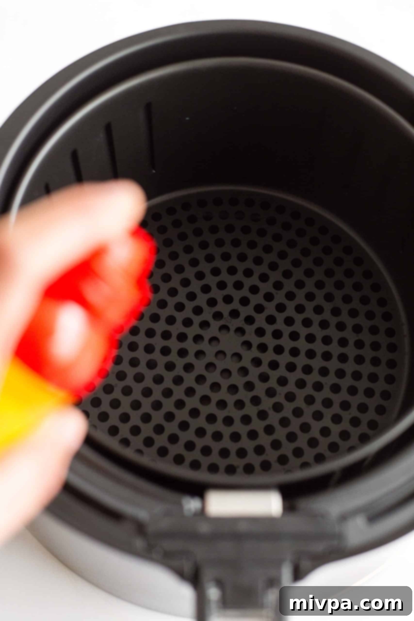 Hand spraying an air fryer basket with non-stick spray.