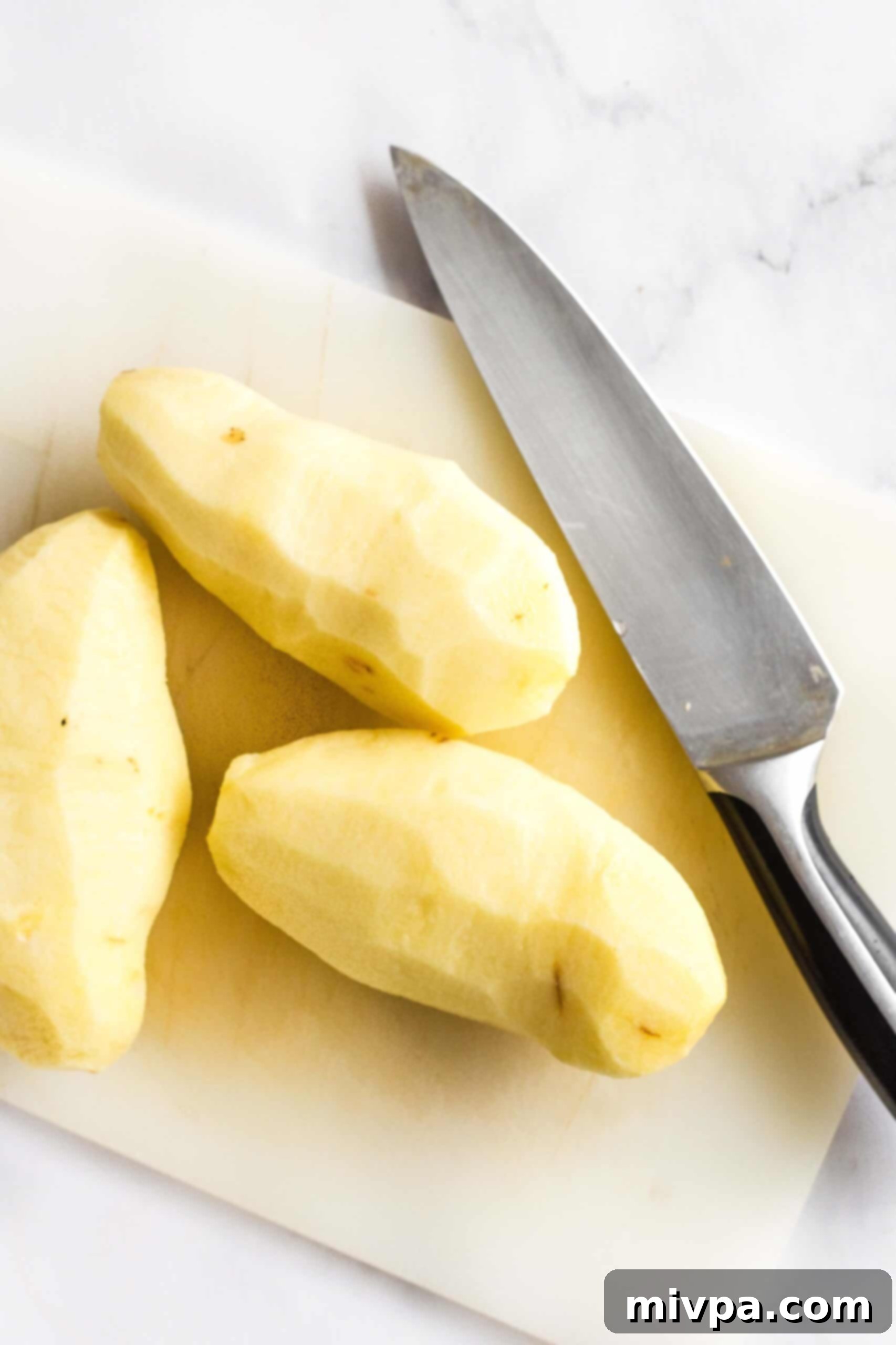 Peeled potatoes and a knife on a chopping board.