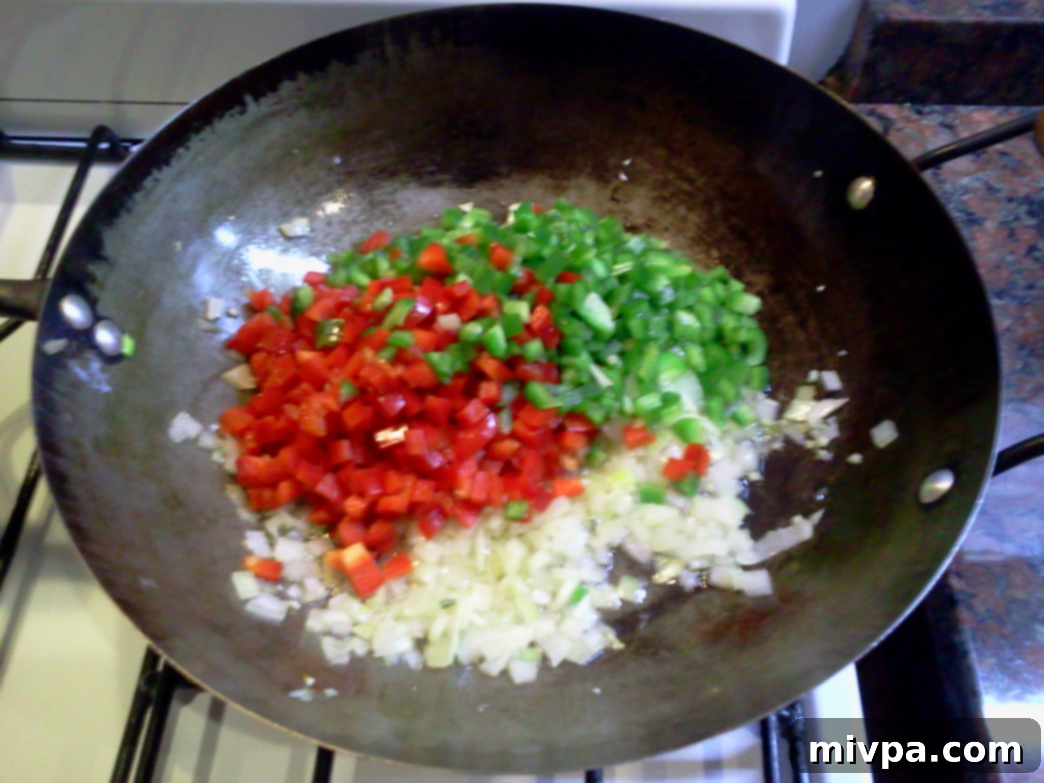 Diced red and green bell peppers are being added to the sautéed onions and garlic in a wok.