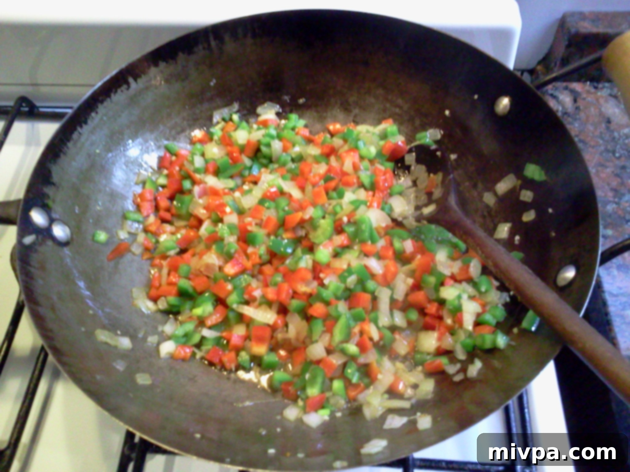 Diced bell peppers are stir-fried in a wok with other aromatics until slightly cooked and softened.