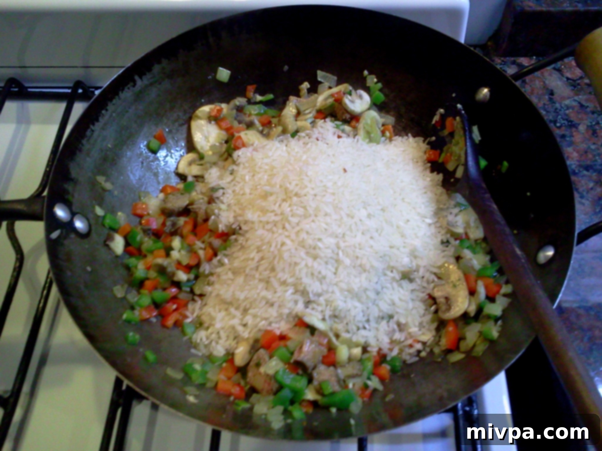Risotto rice is added to the wok with the sautéed vegetables and is being stirred to toast the grains.