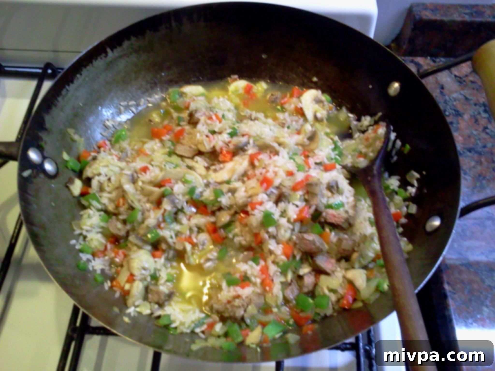 White wine is poured into the wok with the rice and vegetables, being stirred to absorb the liquid.