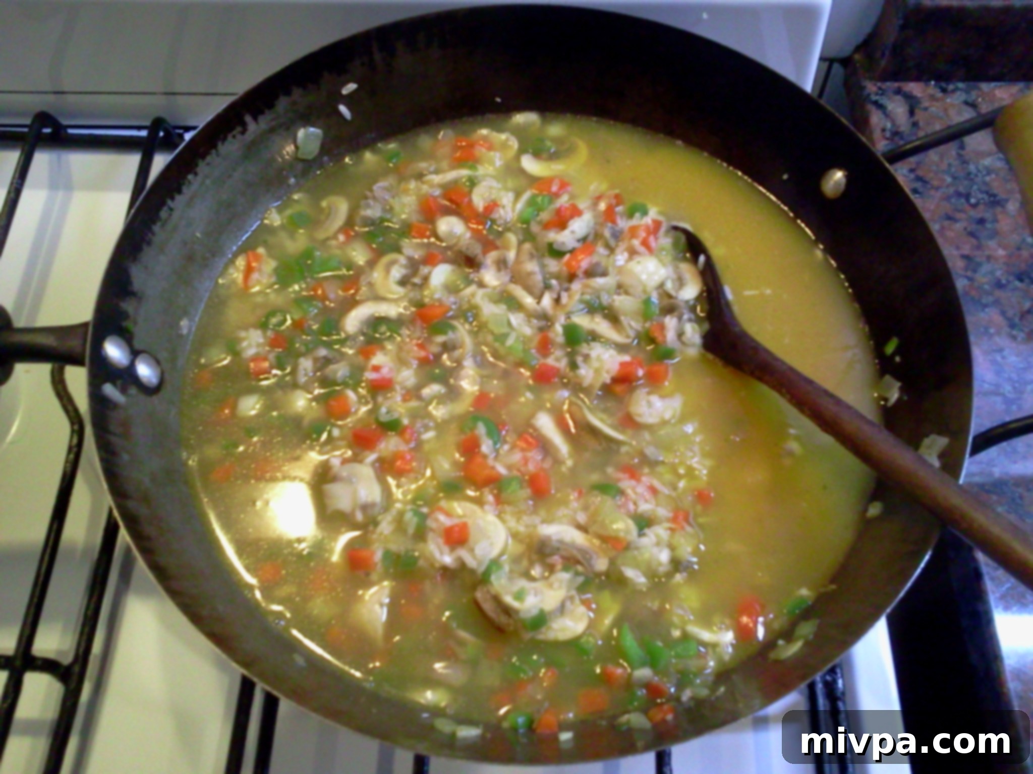 Warm beef stock is being added to the risotto rice in the wok, with continuous stirring to develop creaminess.