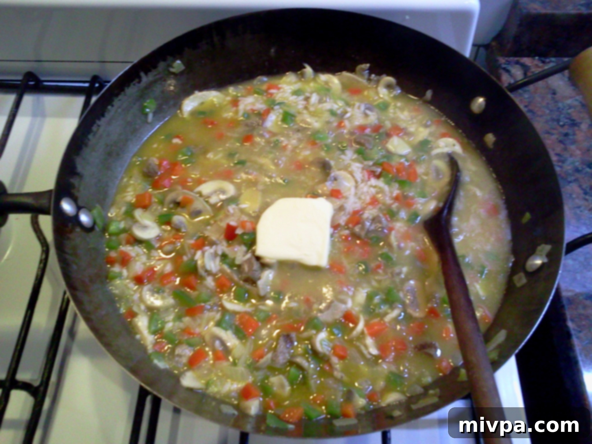 A pat of butter is melting into the cooked risotto, being stirred in for richness and a creamy finish.