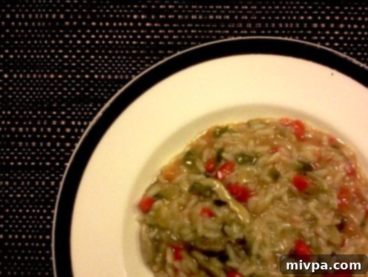 A bowl of hot Spring Vegetable Risotto, garnished with freshly grated cheese and a sprig of fresh herbs, ready to be enjoyed.