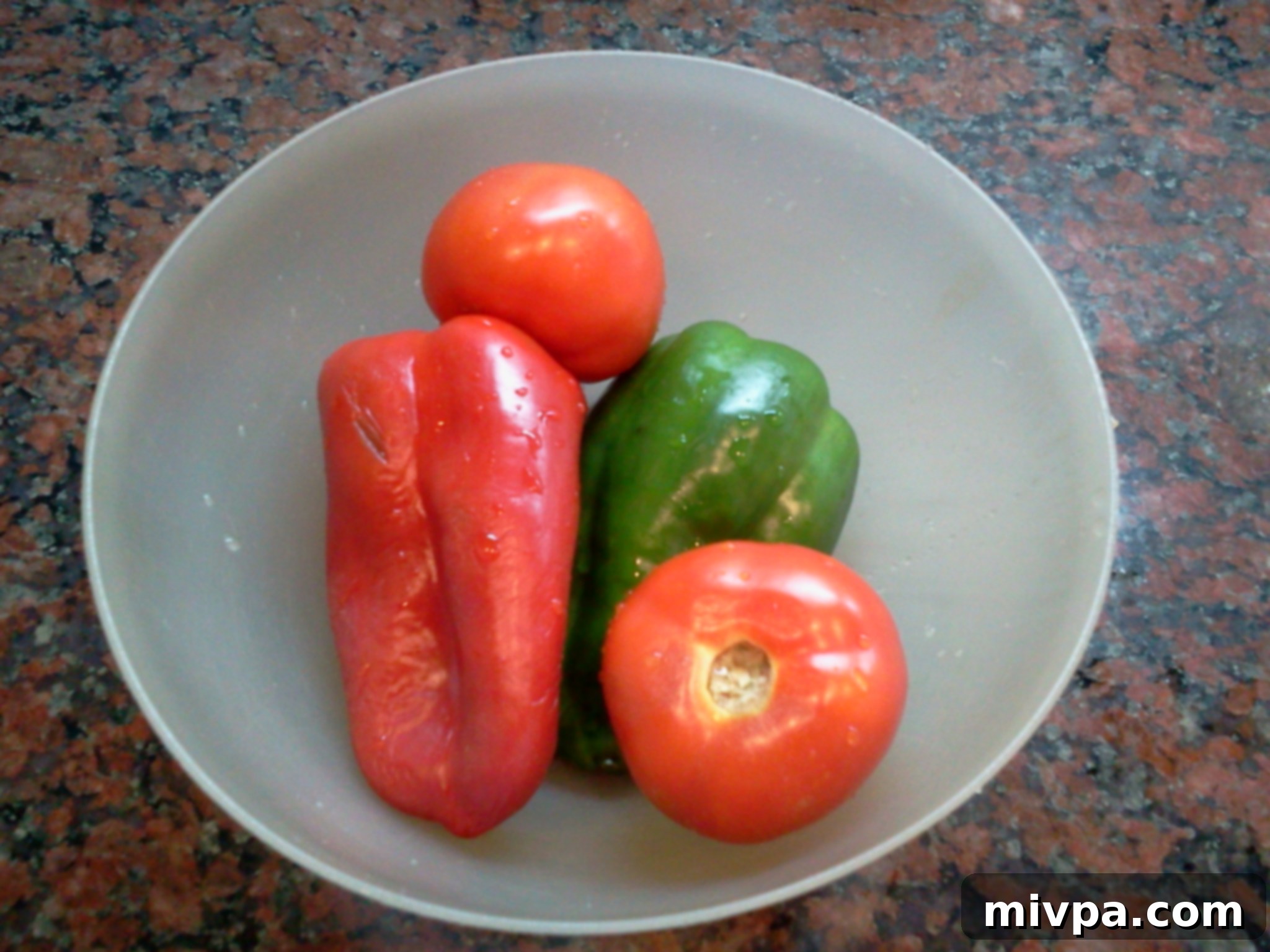 Fresh red and green bell peppers next to ripe red tomatoes, ready for chopping and dicing.