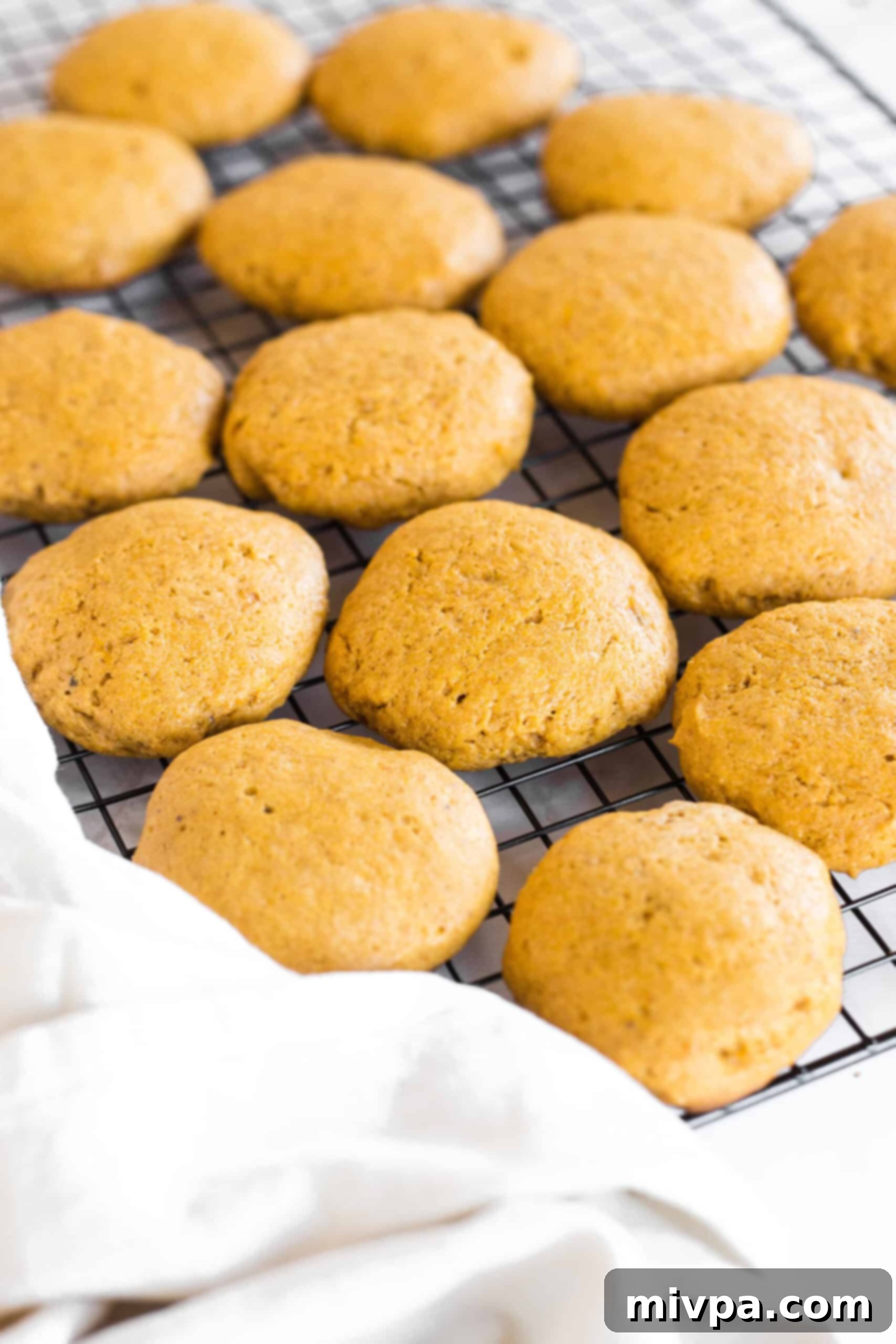 Soft pumpkin cookies on a wire rack with a kitchen towel.