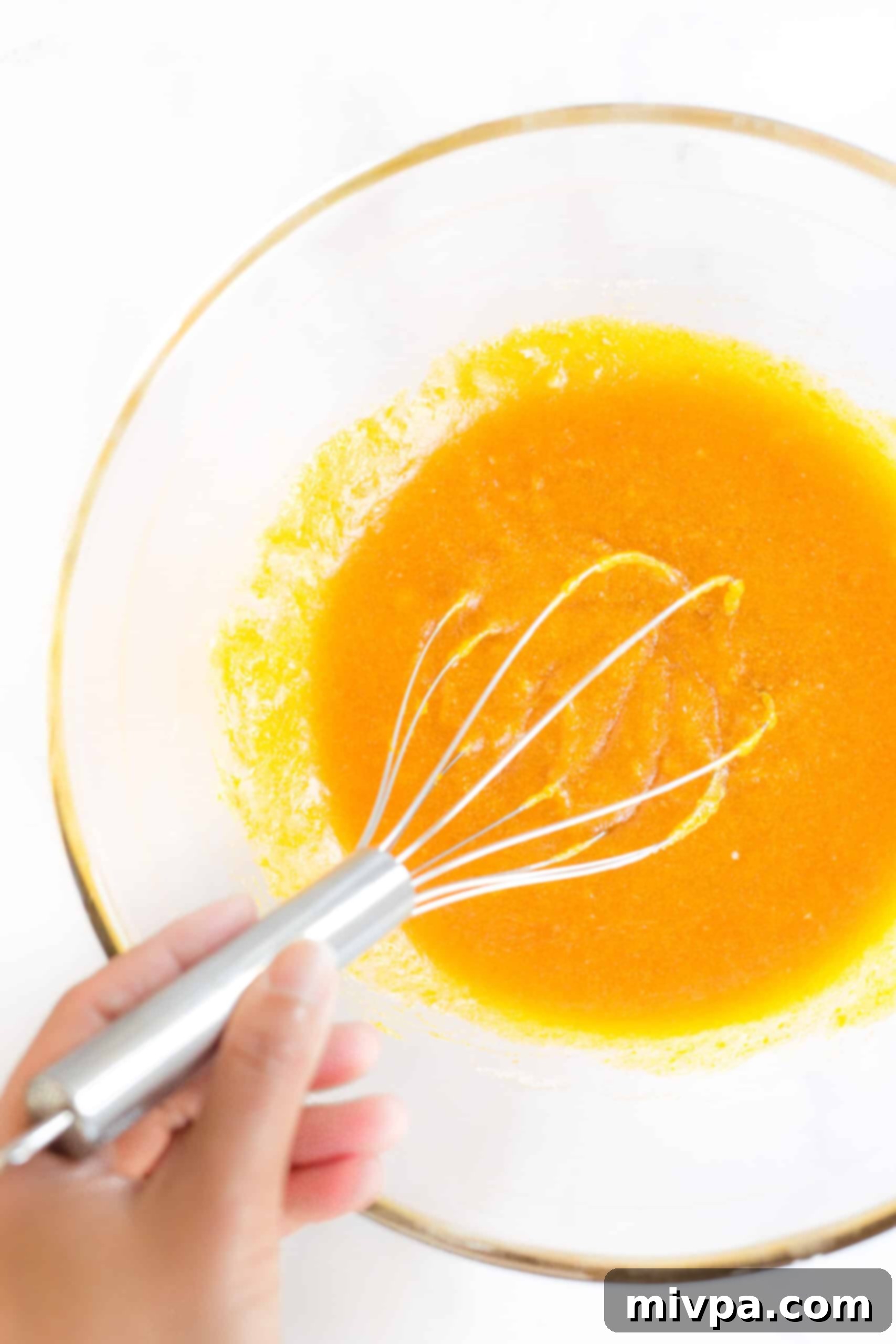 Whisking wet ingredients in a large glass bowl.