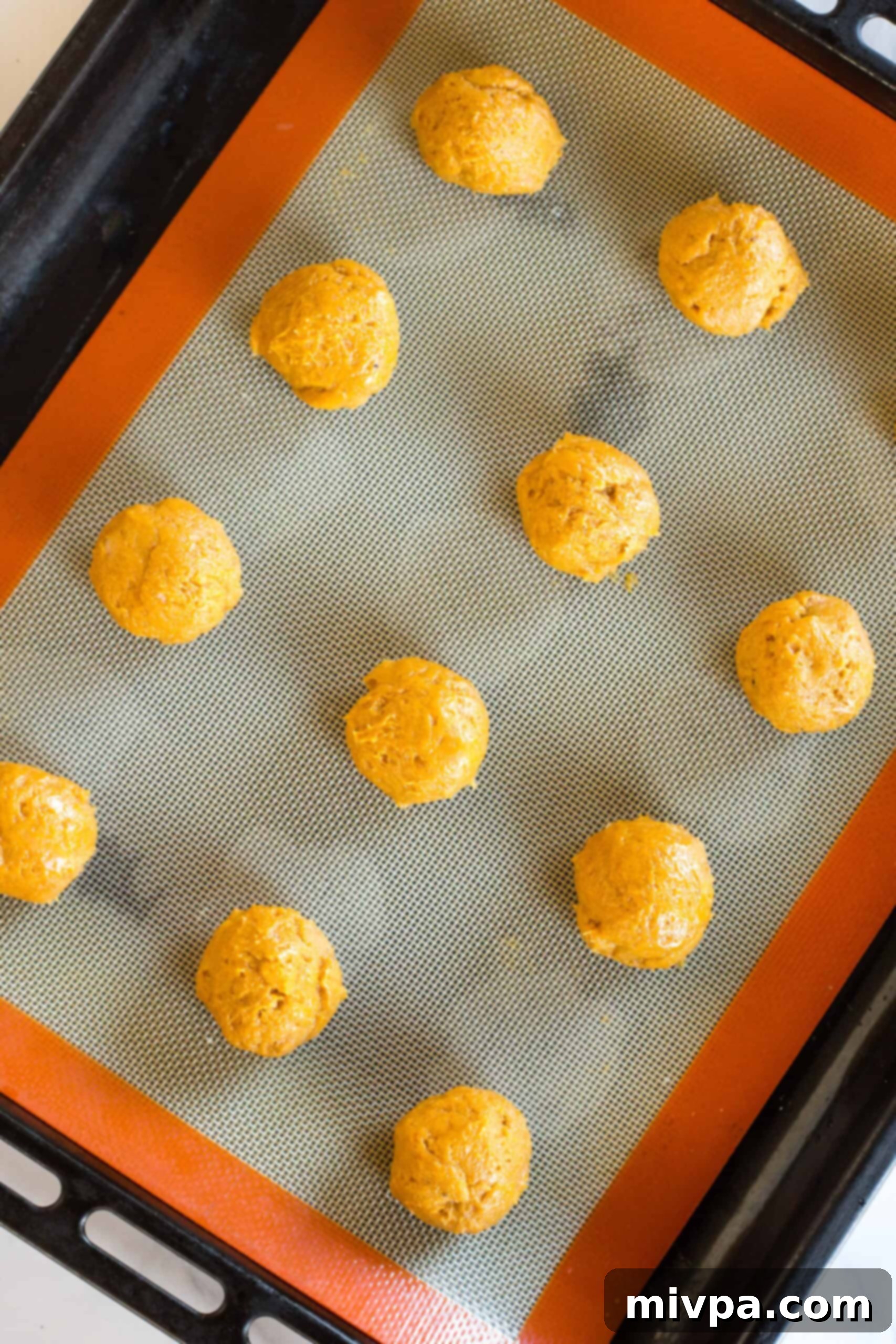 Pumpkin dough balls on a silpat-lined baking sheet.