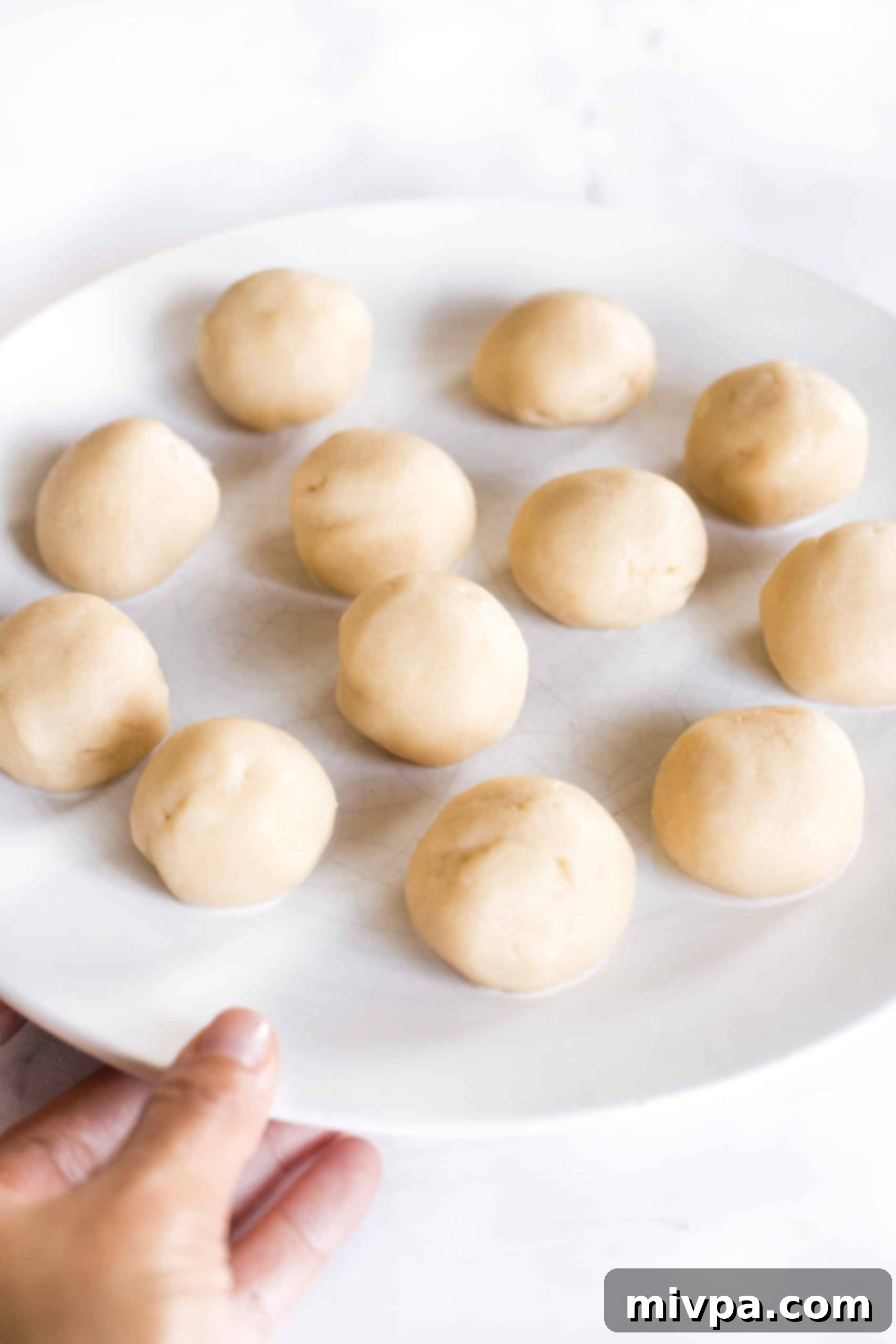 Rolled balls of cookie dough resting on a white plate, ready for the next step.
