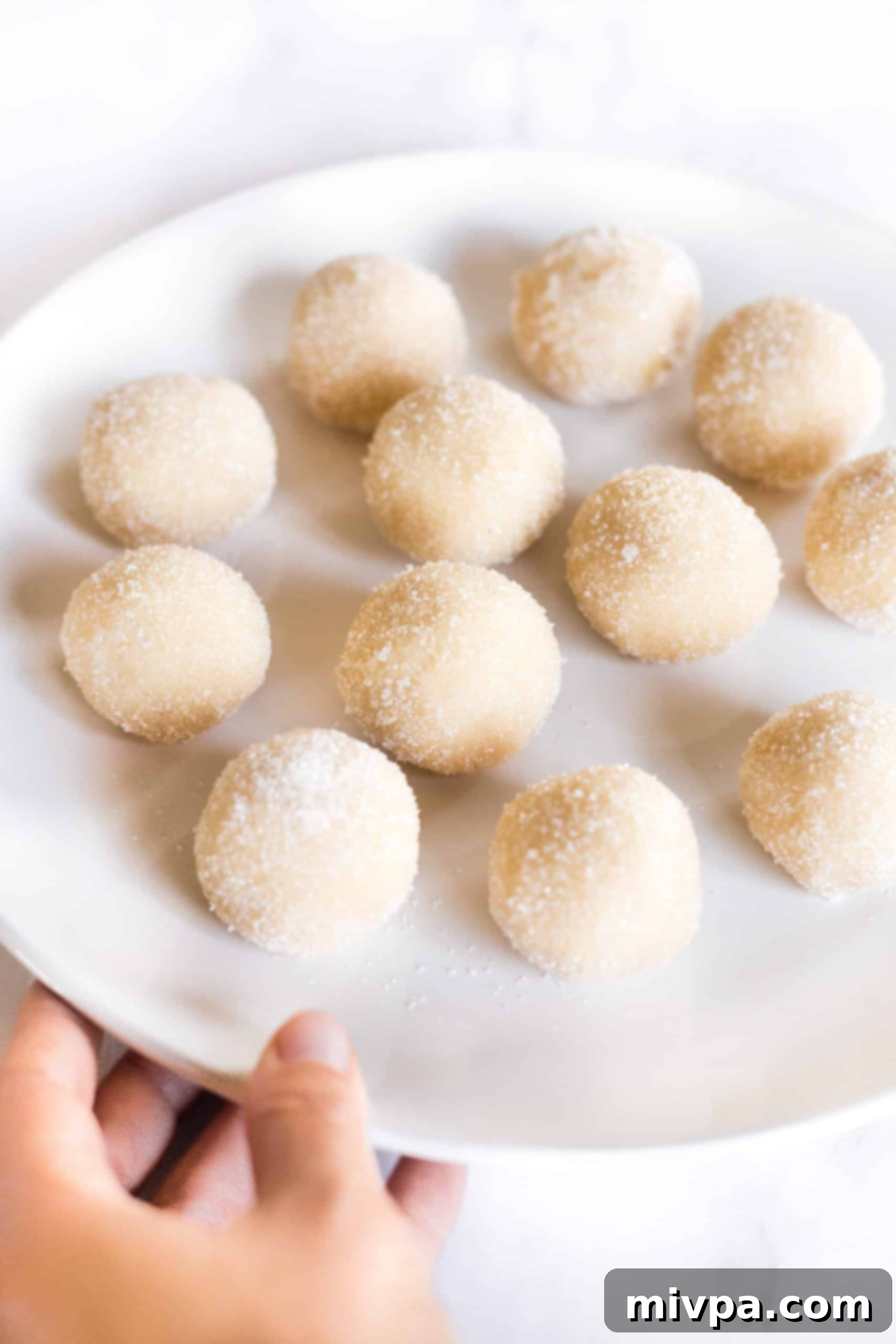 Sugar coated cookie dough balls arranged on a white plate, ready for chilling.