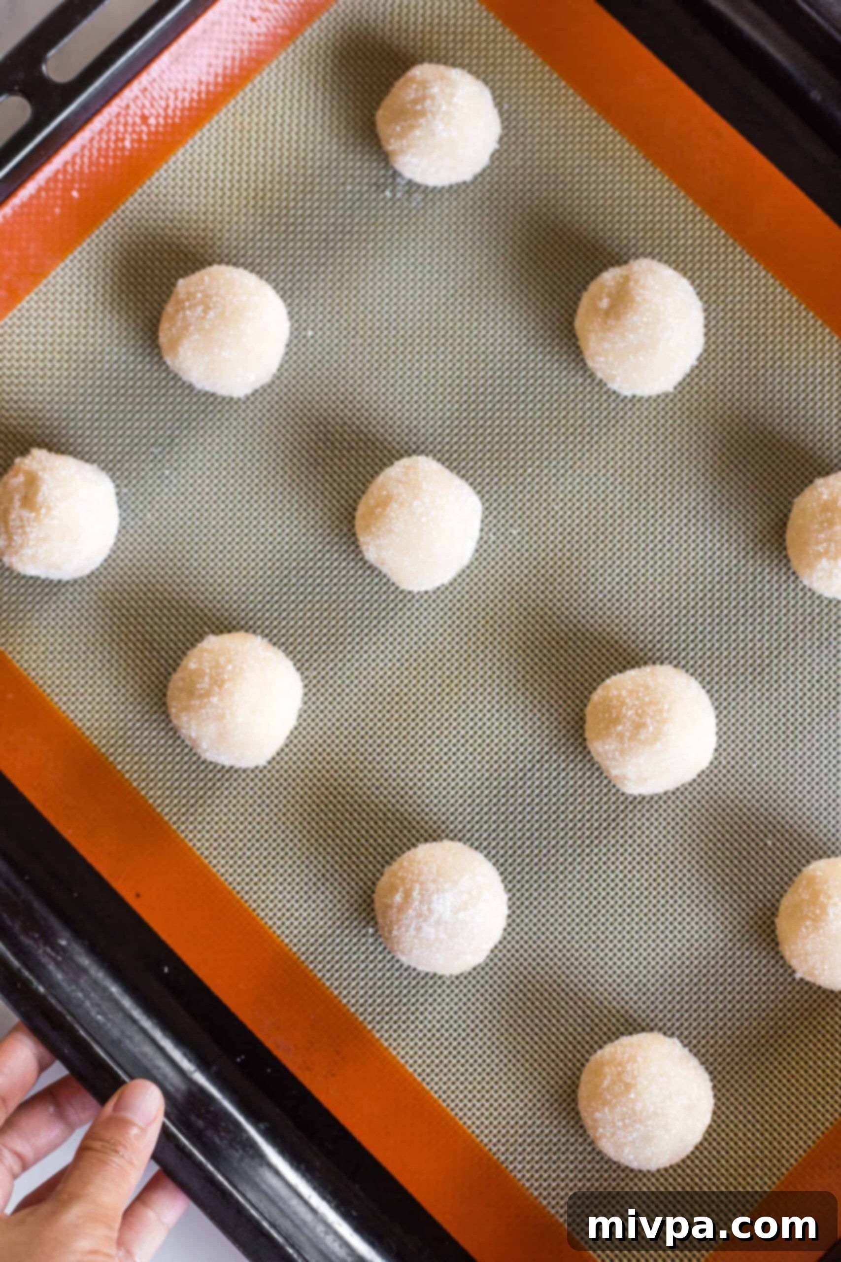 Sugar cookie dough balls spaced out on a silpat-lined baking sheet.