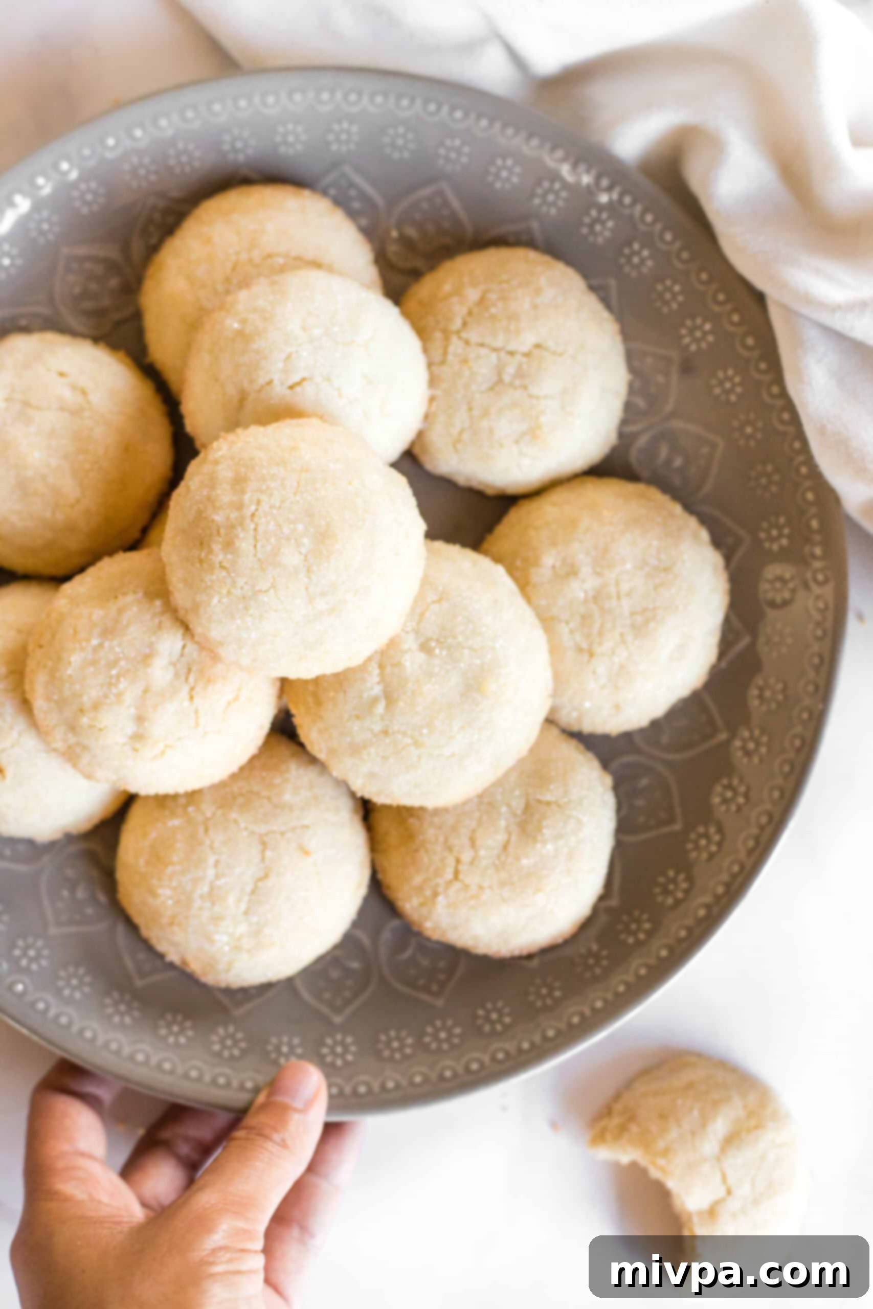 A hand reaching for a plate piled high with freshly baked sugar cookies.