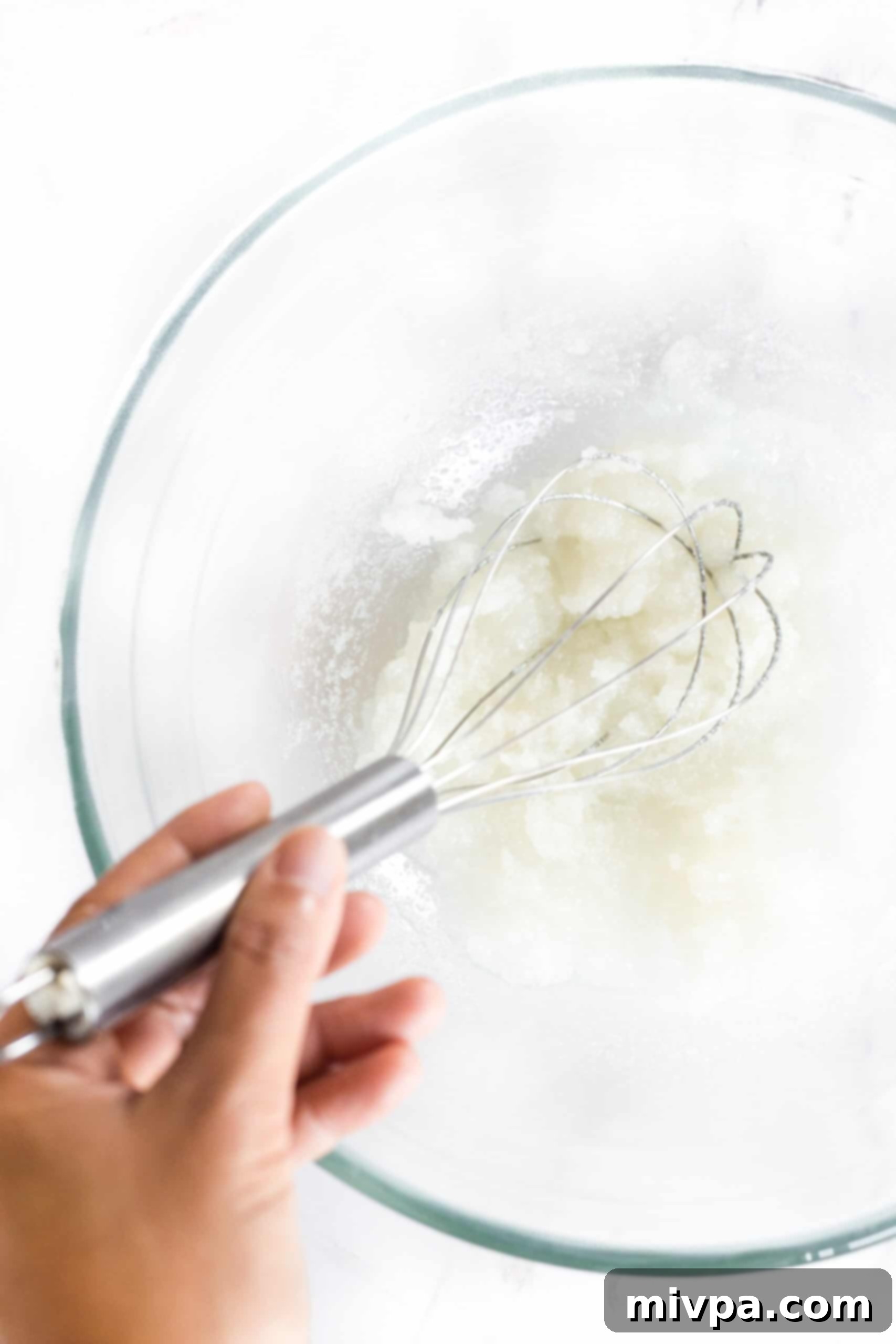 Creaming sugar and coconut oil together in a glass mixing bowl.
