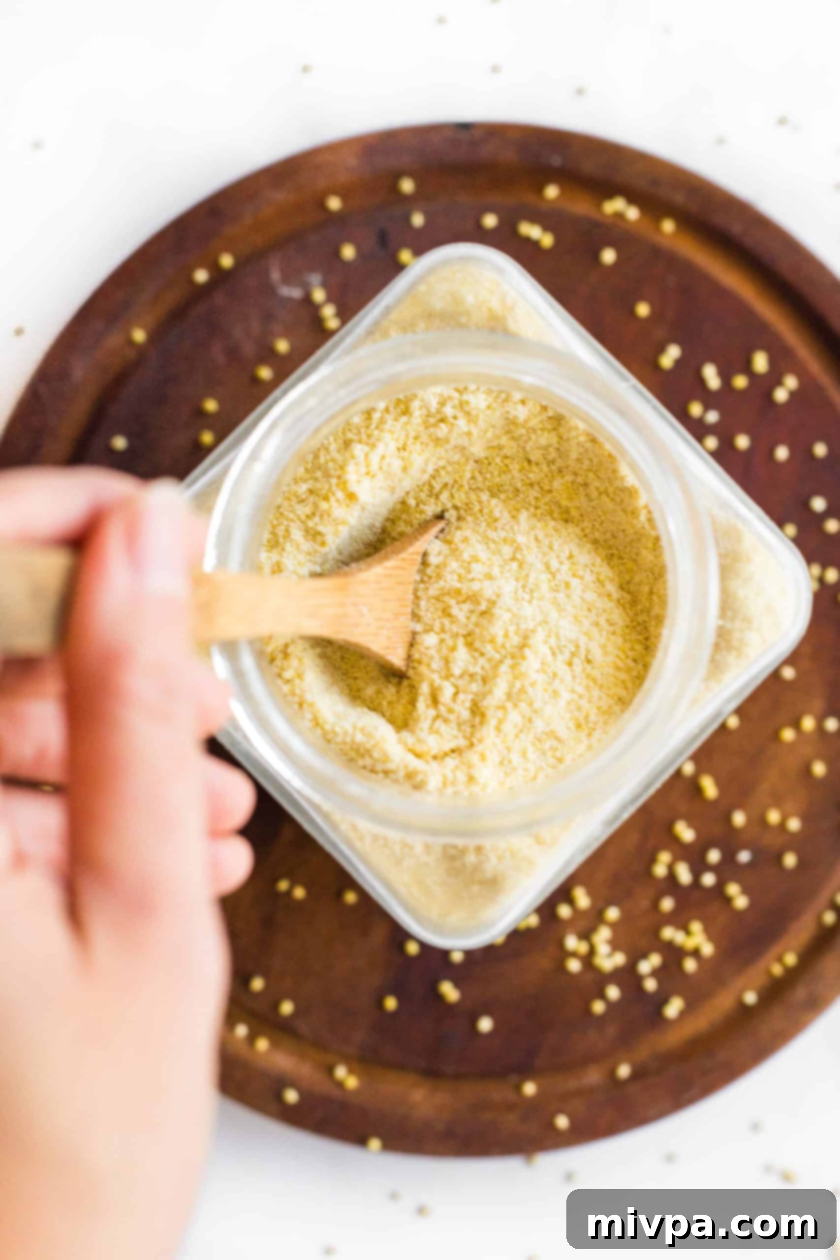 Holding a wooden spoon in a jar of homemade millet flour.