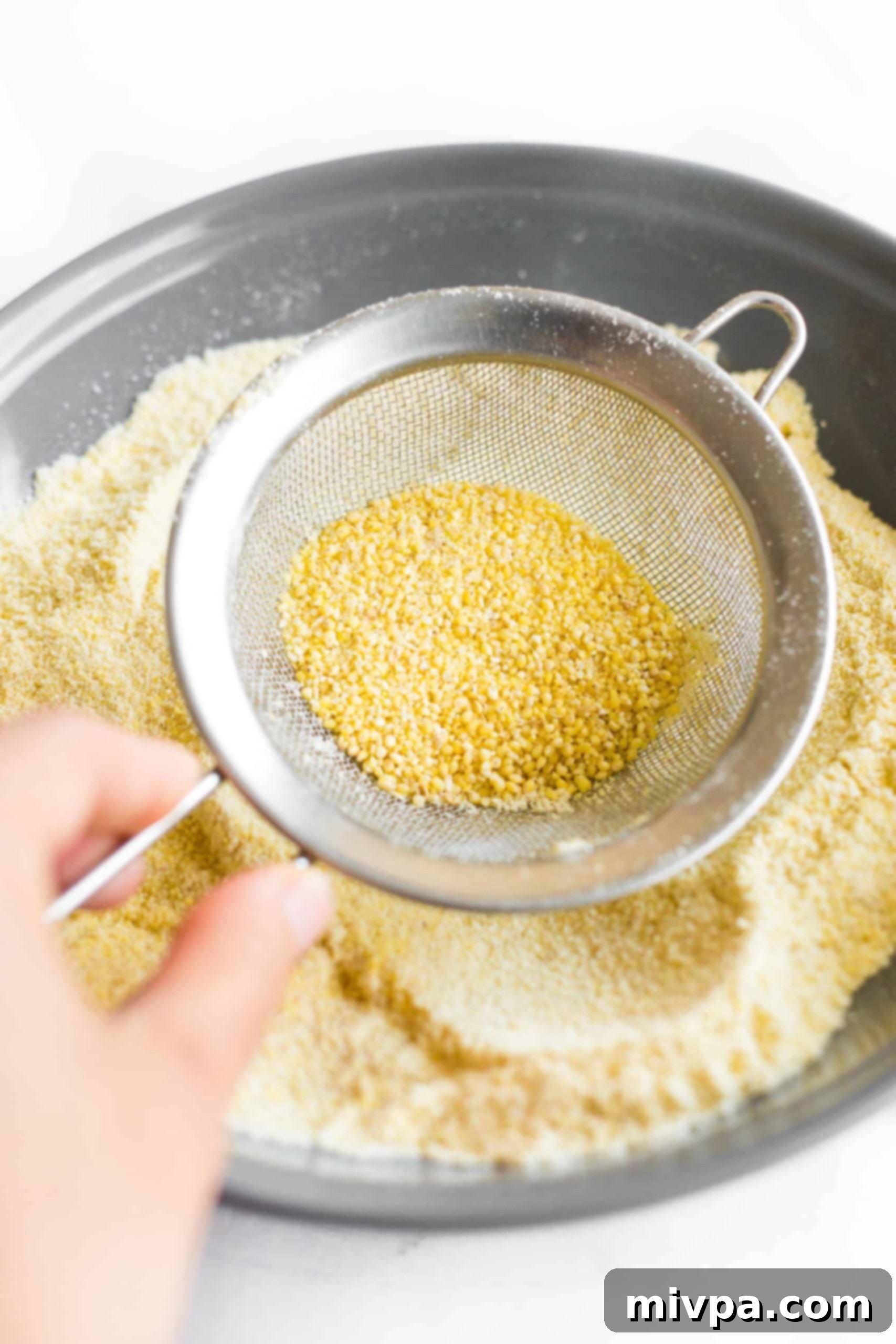 Sifting millet flour through a sieve into a grey bowl.