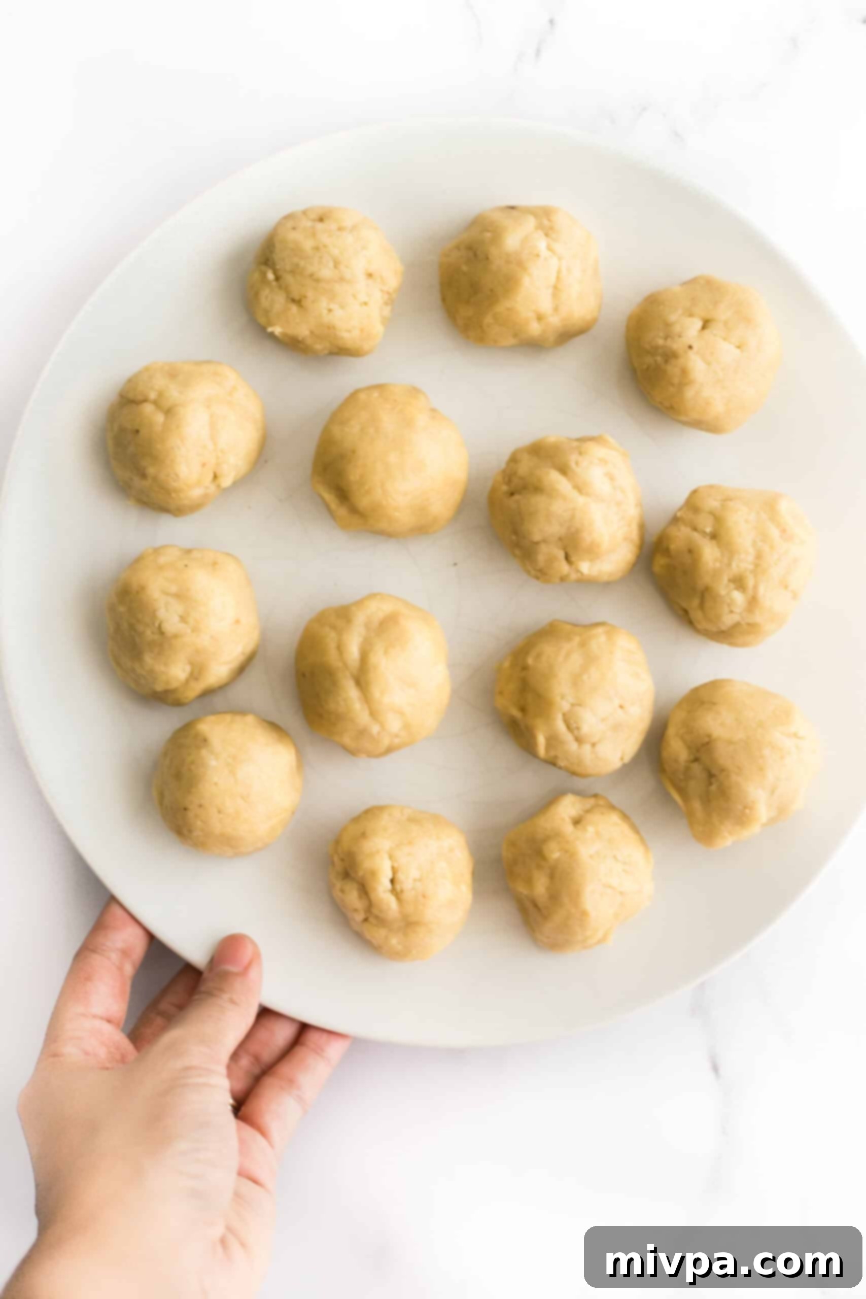 Easy Cashew Nut Cookies Recipe (Gluten-Free, Dairy-Free) - Rolling dough balls Hand holding a plate full of perfectly shaped cashew cookie dough balls, ready for baking.