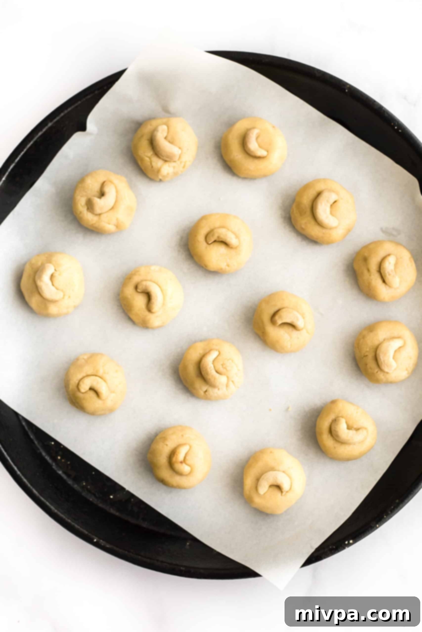 Easy Cashew Nut Cookies (Gluten-Free, Dairy-Free) - Ready for oven Balls of cookie dough, slightly flattened and topped with cashew halves, arranged on a parchment-lined baking sheet.