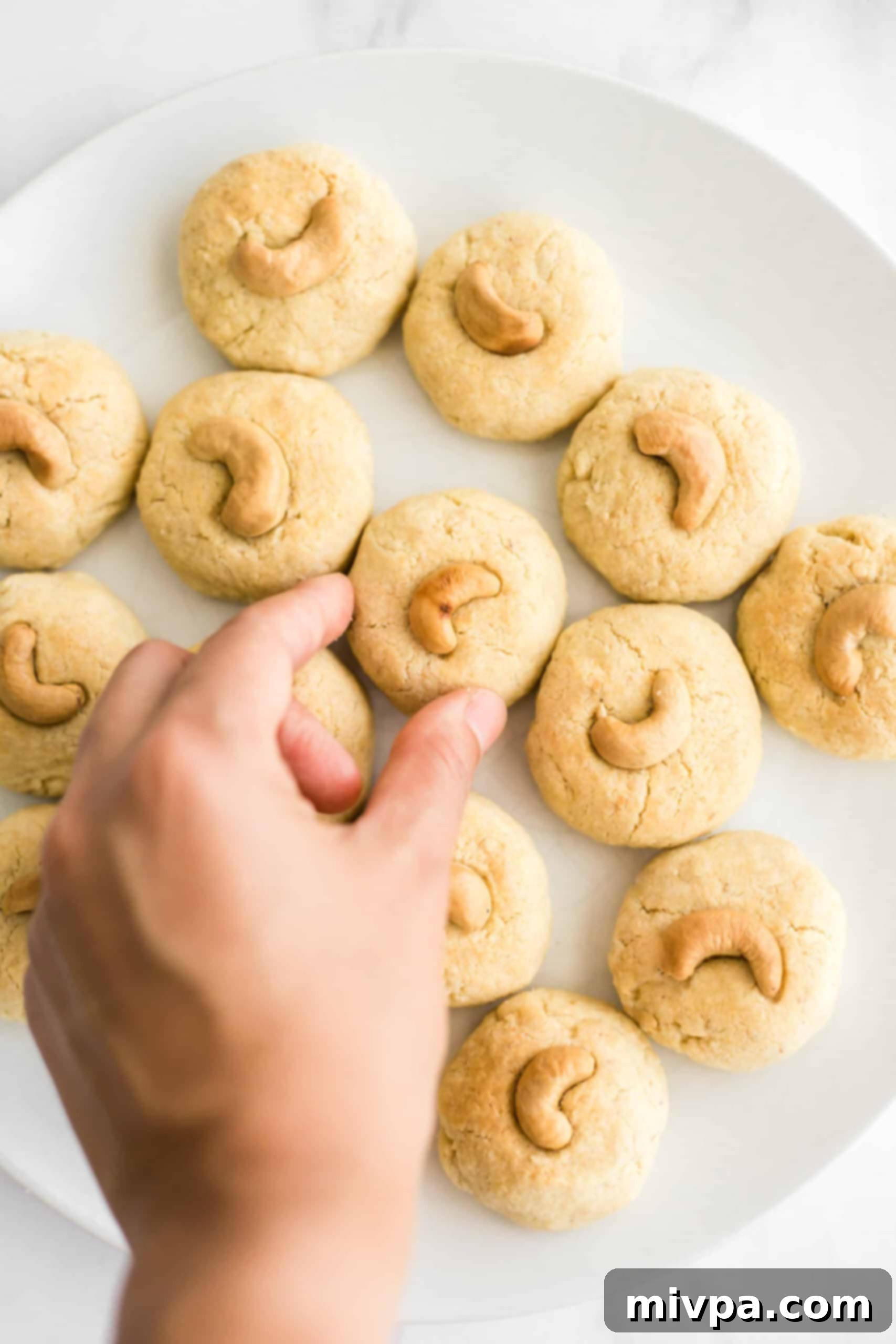 Gluten-Free Cashew Nut Cookies (Dairy-Free) - Freshly baked Hand reaching for a freshly baked, gluten-free cashew nut cookie, golden brown and delicious.