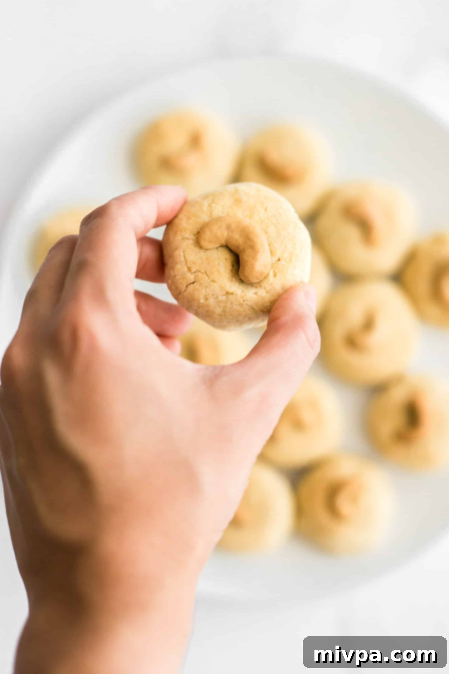 Easy Cashew Nut Cookies (Gluten-Free, Dairy-Free) - A delicious treat Hand holding up a single gluten-free cashew nut cookie, showcasing its golden color and perfect shape against a blur background.