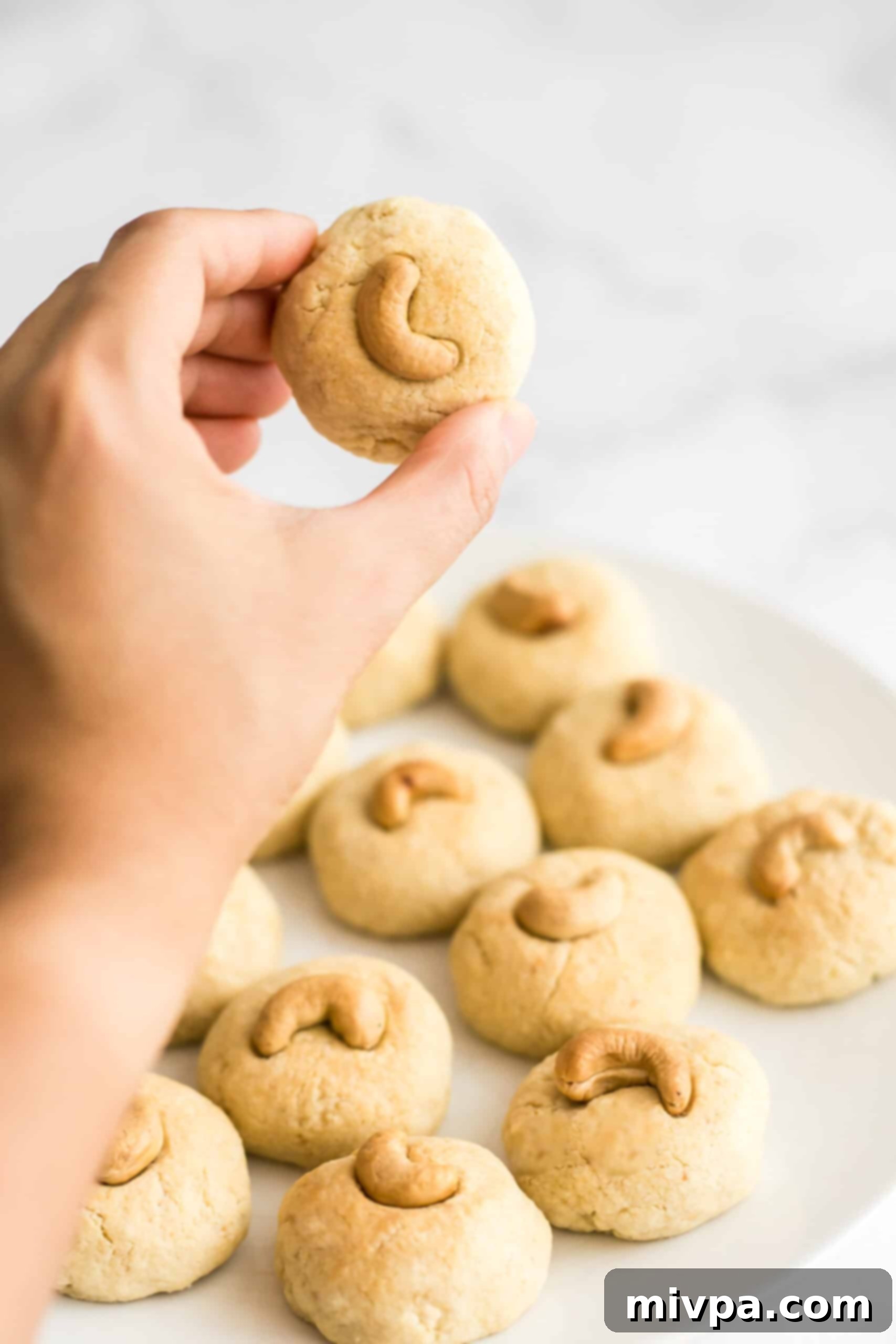 Easy Cashew Nut Cookies Recipe (Gluten-Free, Dairy-Free) - A perfect bite-sized treat Close-up of a hand holding a single gluten-free cashew cookie, showing its texture and cashew topping.