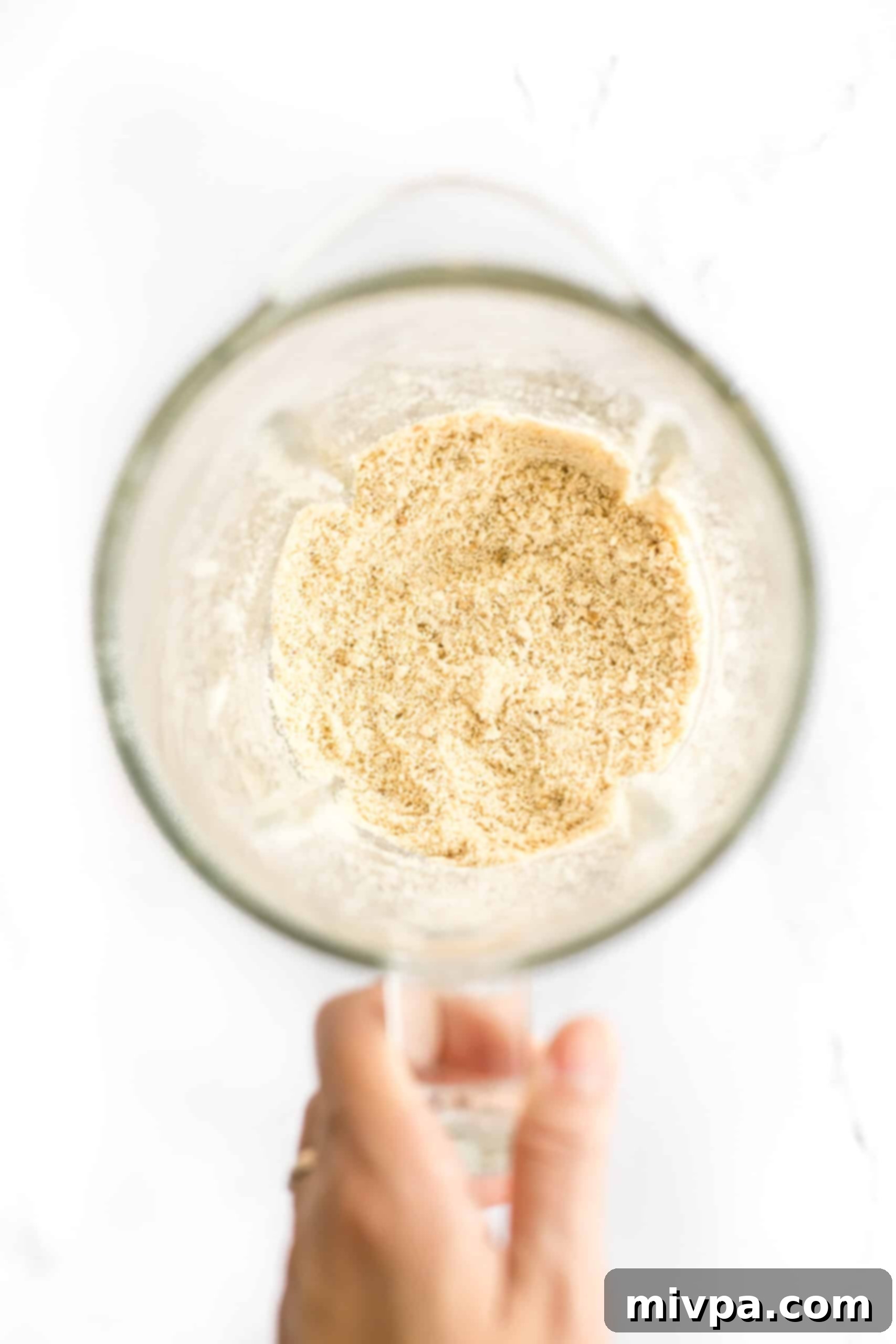 Gluten-Free Cashew Nut Cookies (Dairy-Free) - Grinding cashews Hand holding a blender with freshly ground cashew flour, showing its fine texture.