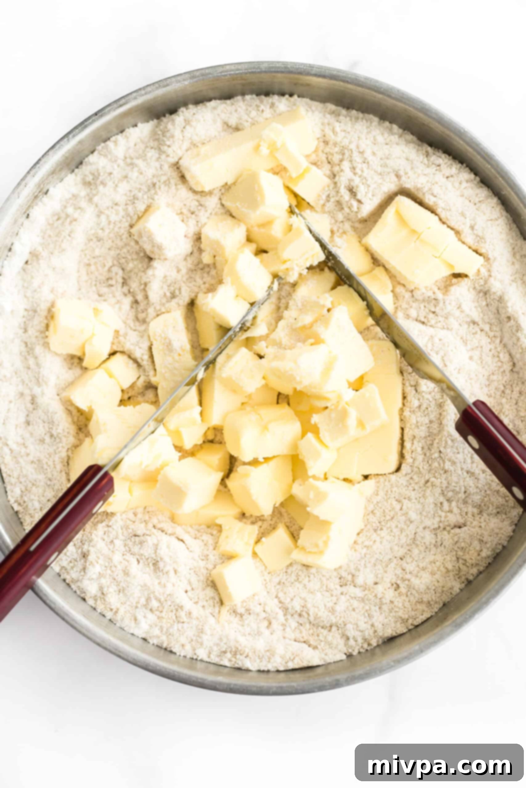 Gluten-Free Dairy-Free Cashew Nut Cookies - Cutting in butter Using two knives to cut cubed dairy-free butter into the flour mixture, creating a sandy texture.