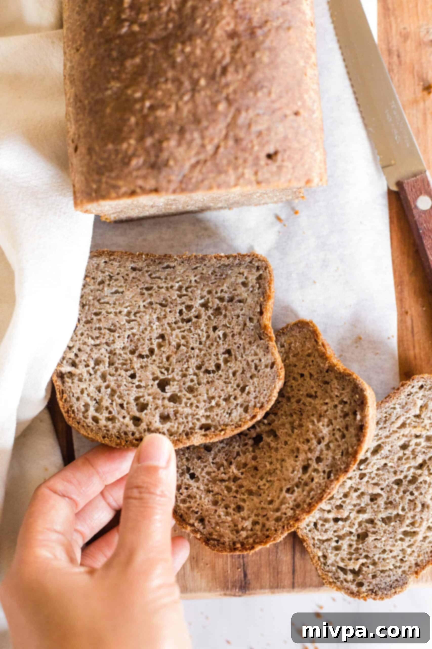 Soft, Fluffy Teff Bread (Gluten-Free, Dairy-Free) Hand reaching for a slice of gluten-free teff bread on wooden board.