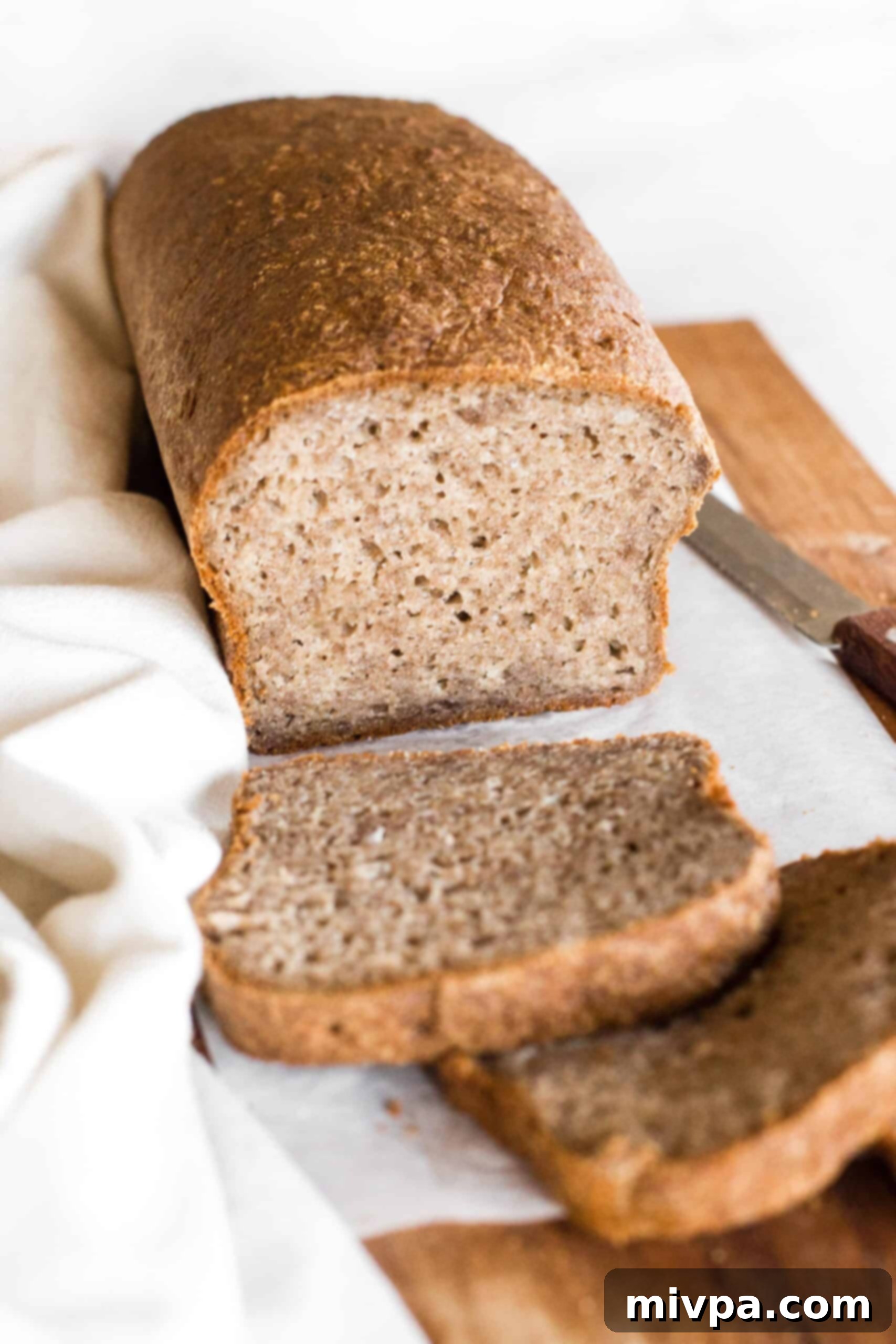 Soft, Fluffy Teff Bread (Gluten-Free, Dairy-Free) Half-sliced loaf of teff flour bread on parchment-lined wooden board.