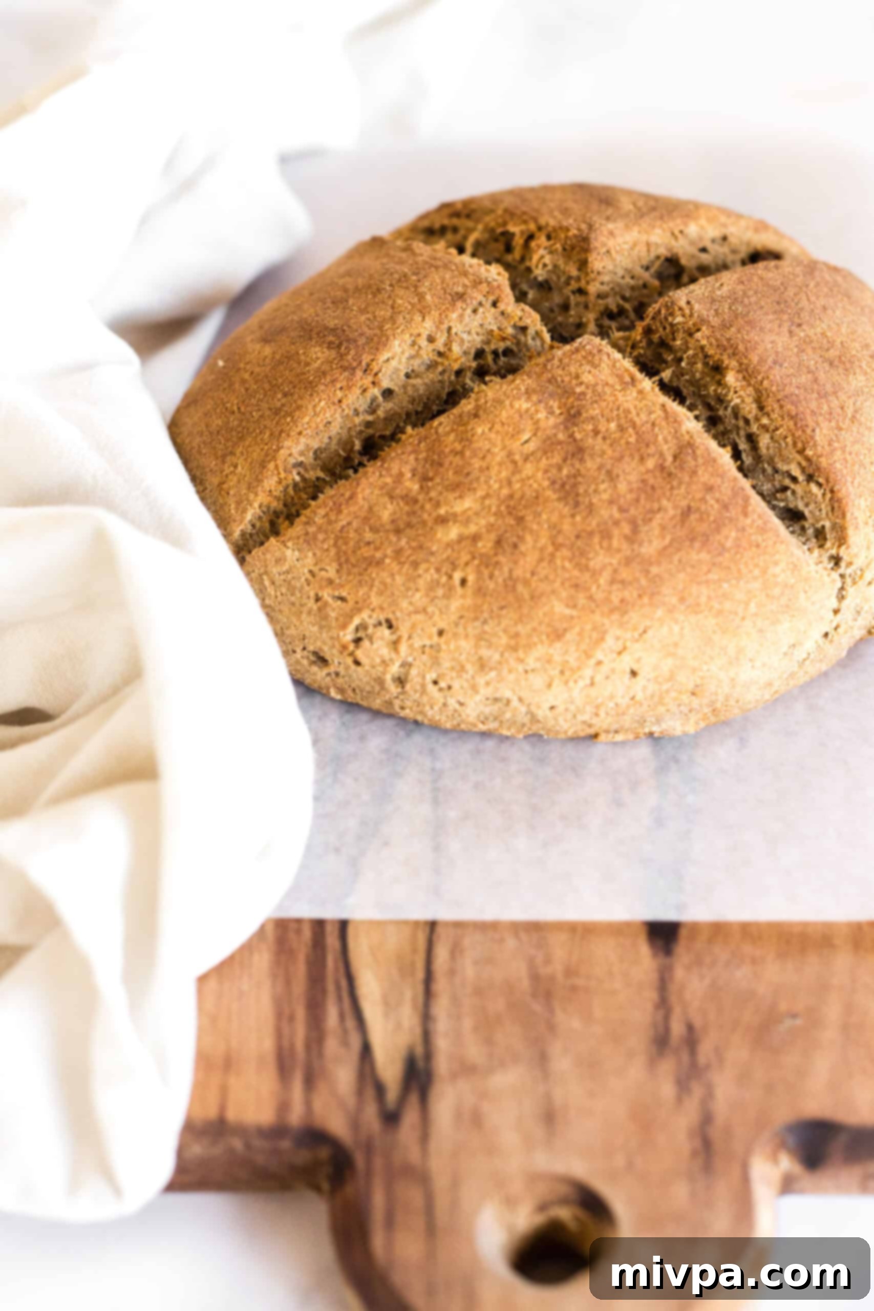 Freshly baked loaf of Irish brown soda bread on parchment-lined wooden board.