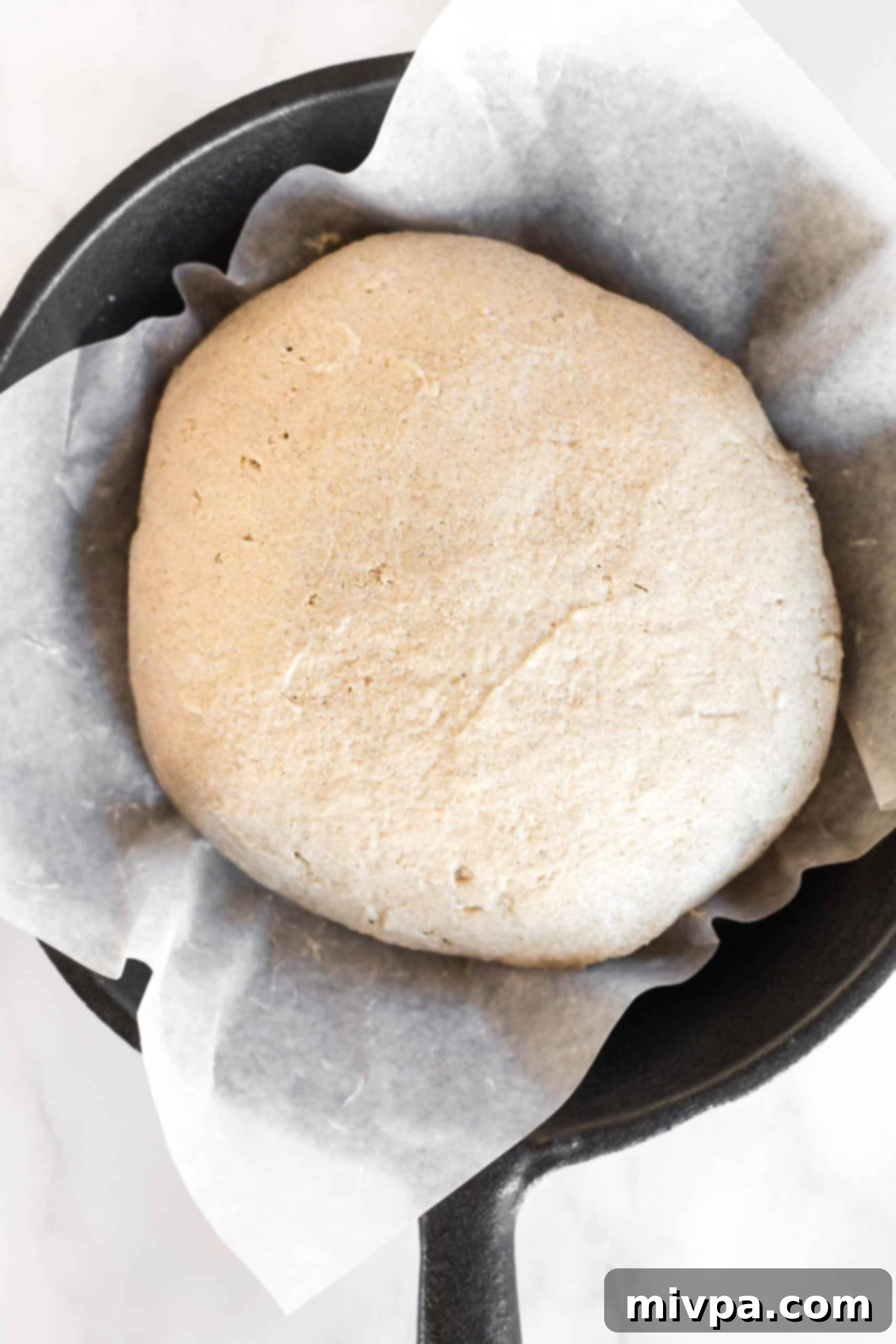 Brown bread dough in parchment-lined cast iron pan