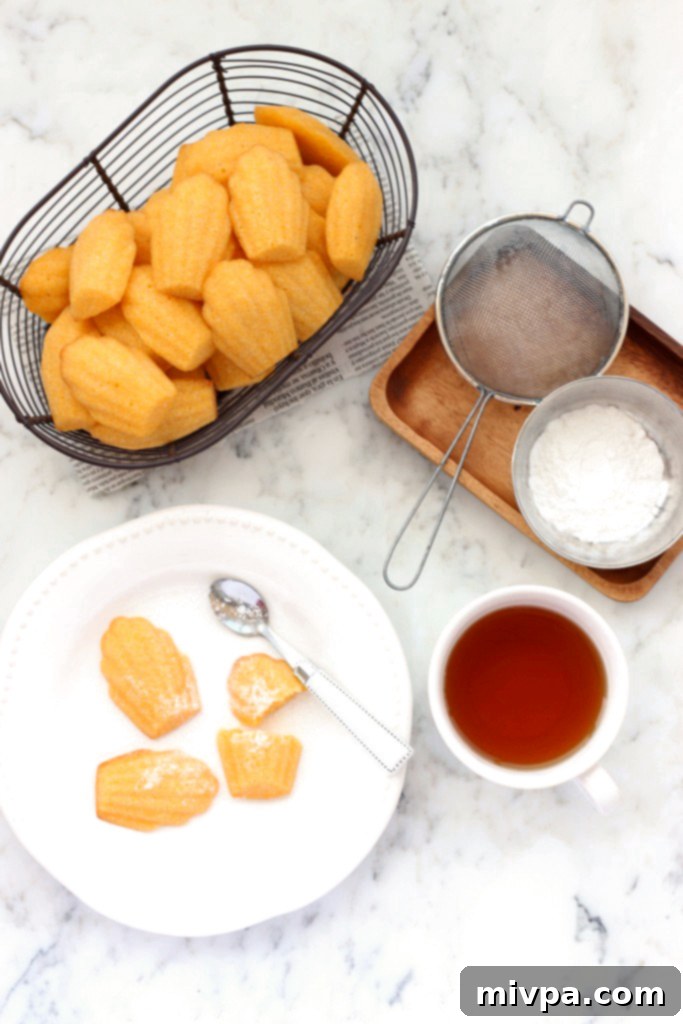 A charming wire basket filled with freshly baked gluten-free cornbread madeleines, beside a cup of tea on a marble board.