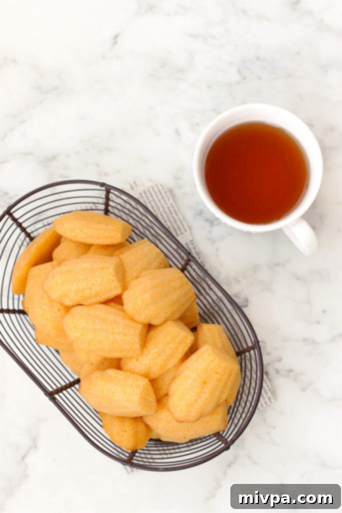 A closer look at a wire basket overflowing with gluten-free cornbread madeleines, with a teacup on a marble board.