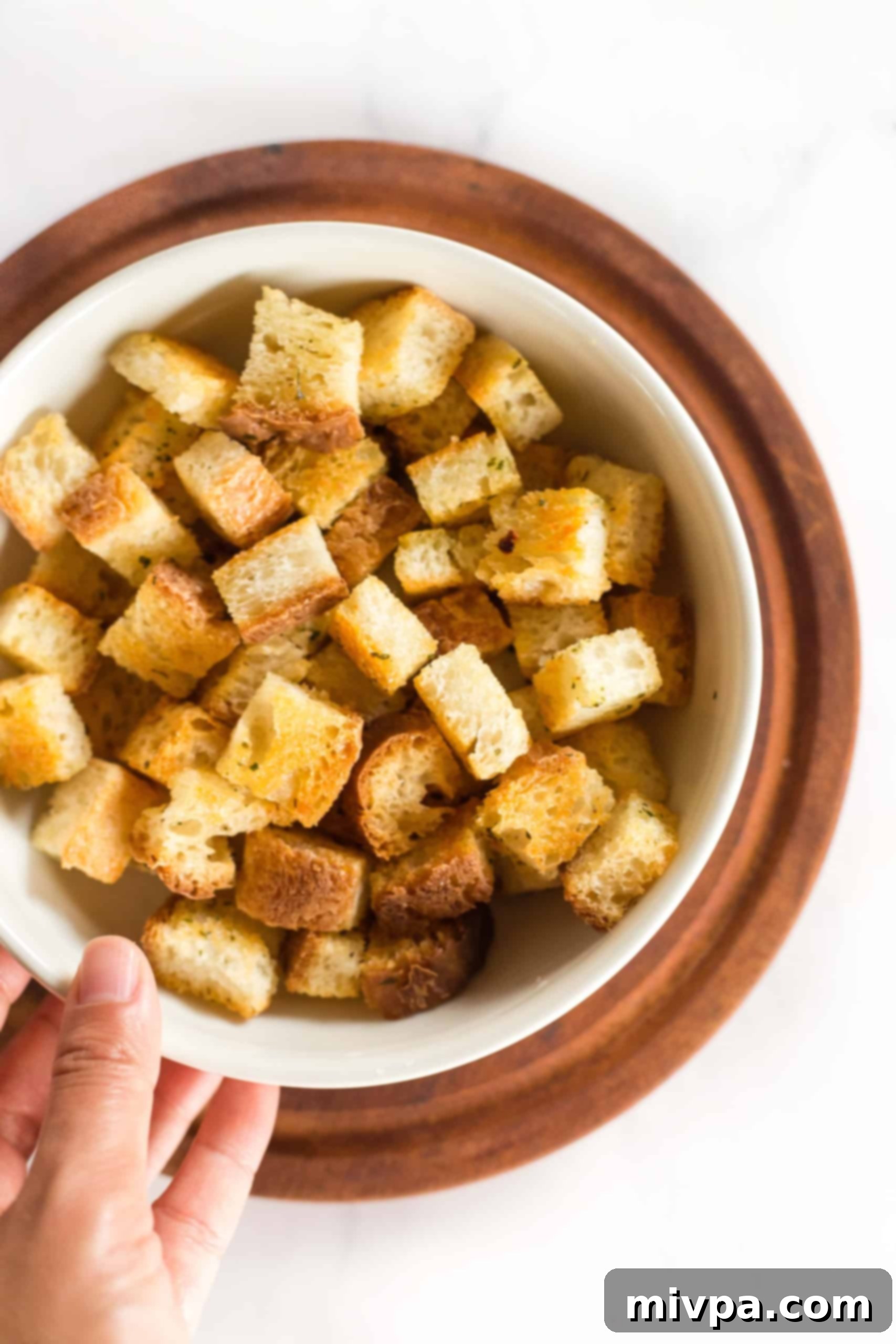 A hand reaching into a white bowl filled with homemade gluten-free croutons, showcasing their golden texture.